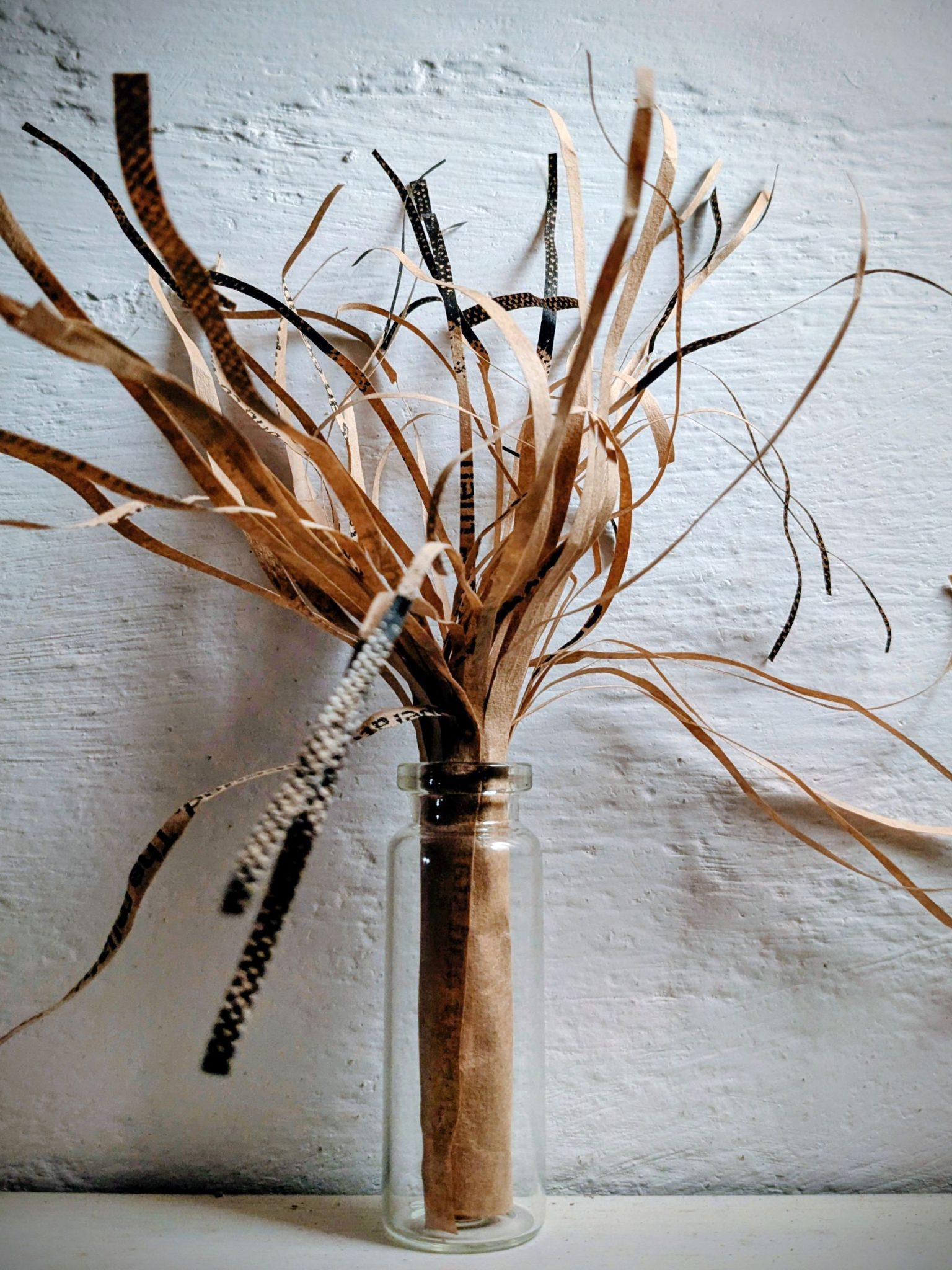 A small glass bottle with an explosion of thin strands of paper coming out from the top