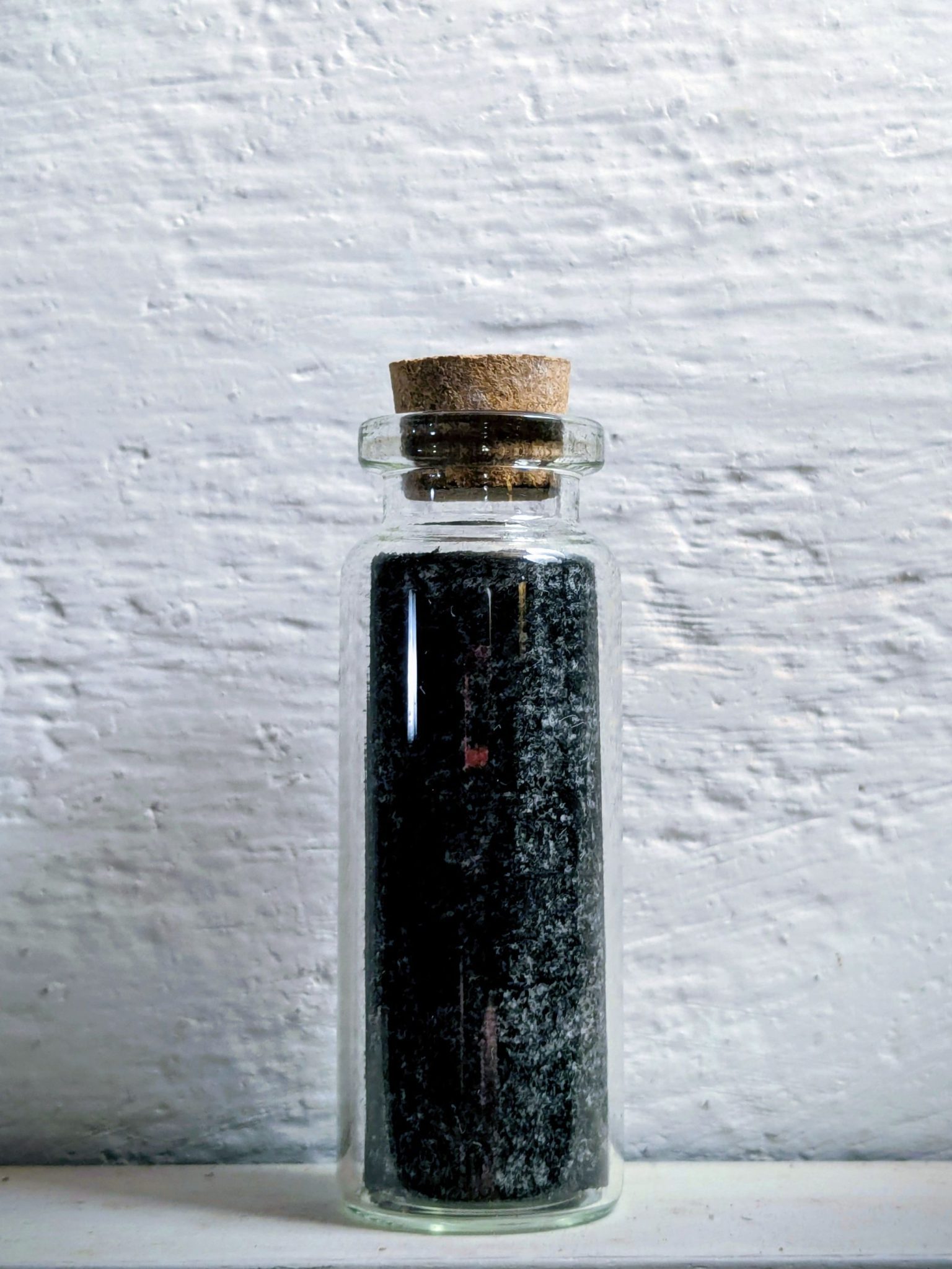 A glass bottle containing a paper on which charcoal has been rubbed, looking like it's filled with something blackt