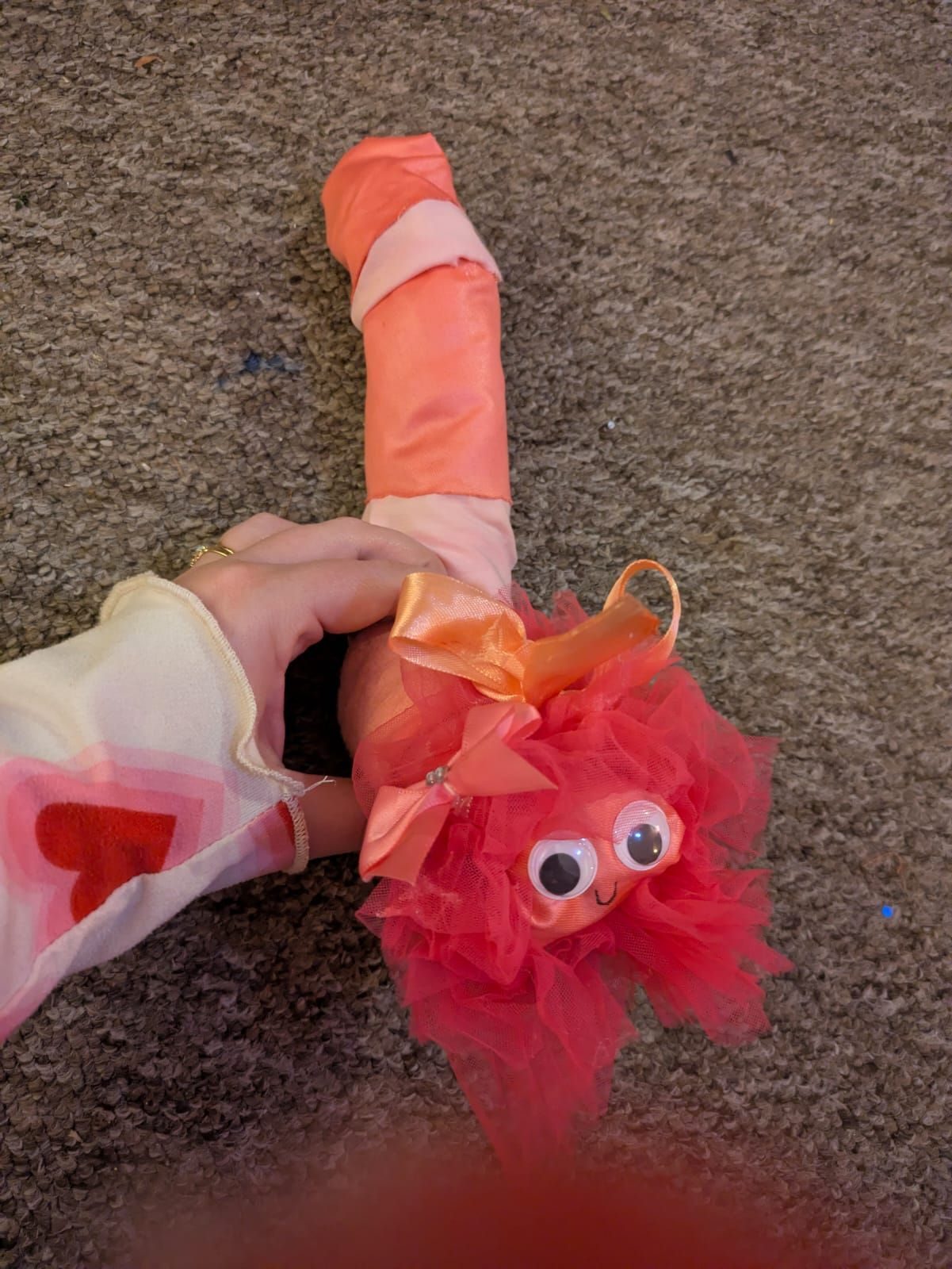 A fabric worm sculpture with pink ruff and bows as well as Googley eyes