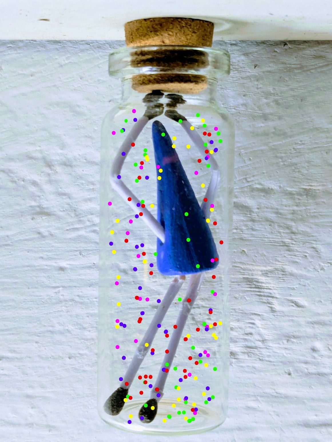 A small glass bottle hangs from above. It contains a small figure and confetti have been drawn inside the bottle