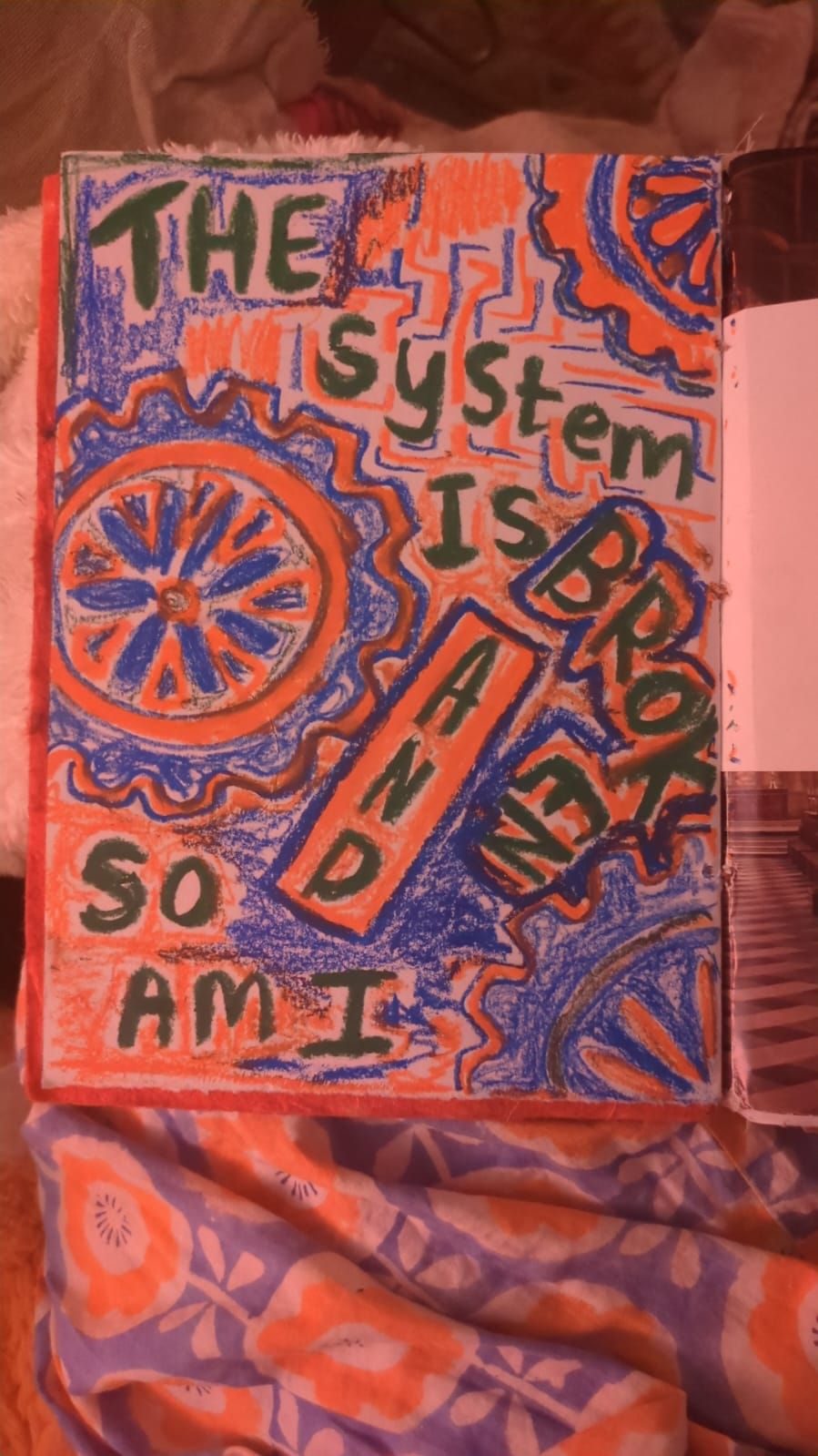 Drawing in wax. Writing on top 'the system is broken and so am I' around it is symbols that are similar to machine cogs and wires