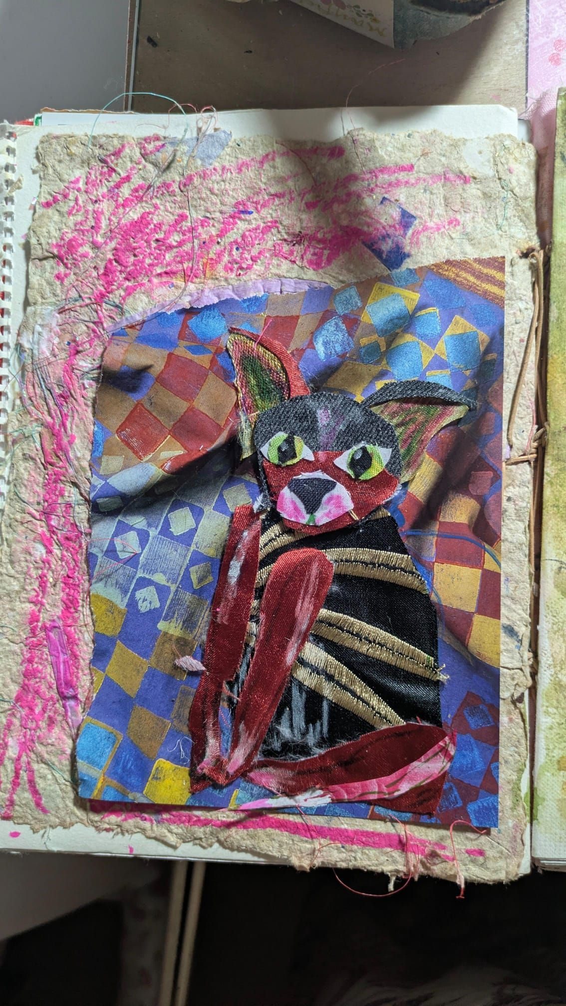 A fabric and paper collage of a badly made cat that looks a bit like a chihuahua but also maybe a fox?