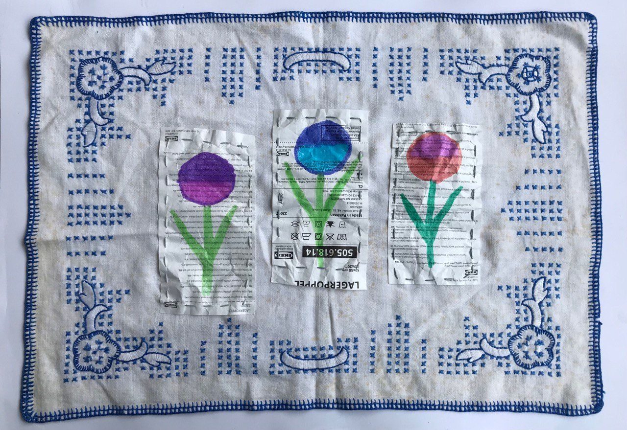 Vintage napkin with blue embroidered edging; three IKEA tags sewn on, with flowers drawn in felt-tip pen.