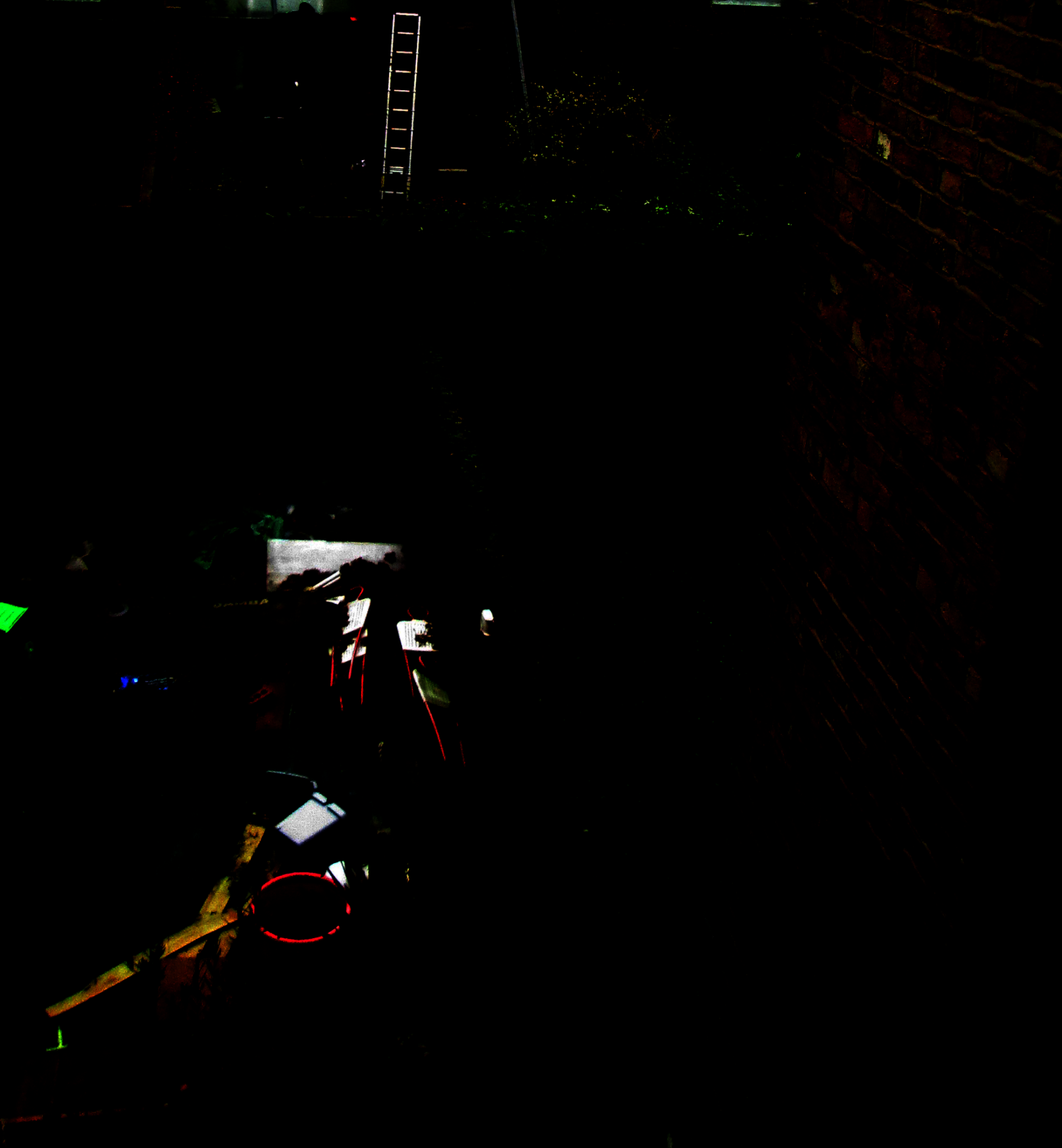 the image is almost totally black, tot eh left is a green shape that abuts the edge of the frame halfway up, blow are to shapes linear, one ends in a round bright scarlet outline, and there are shapes that might be related that are white, the one to the left being almost rectangular, cross by a black line, , above to the left is a blue glimpse of light? LED?, to the right are several straight lines that appear to have white rectangular shapes attached or integral to them and above that appears the outlines of what might be a hedge or a bush, and a tubular shape? thrown into relief to what appears a skyline of clouds trapped by the black, way above this reaching to the top centre of the frame is a ladder to what could be red or green light?
