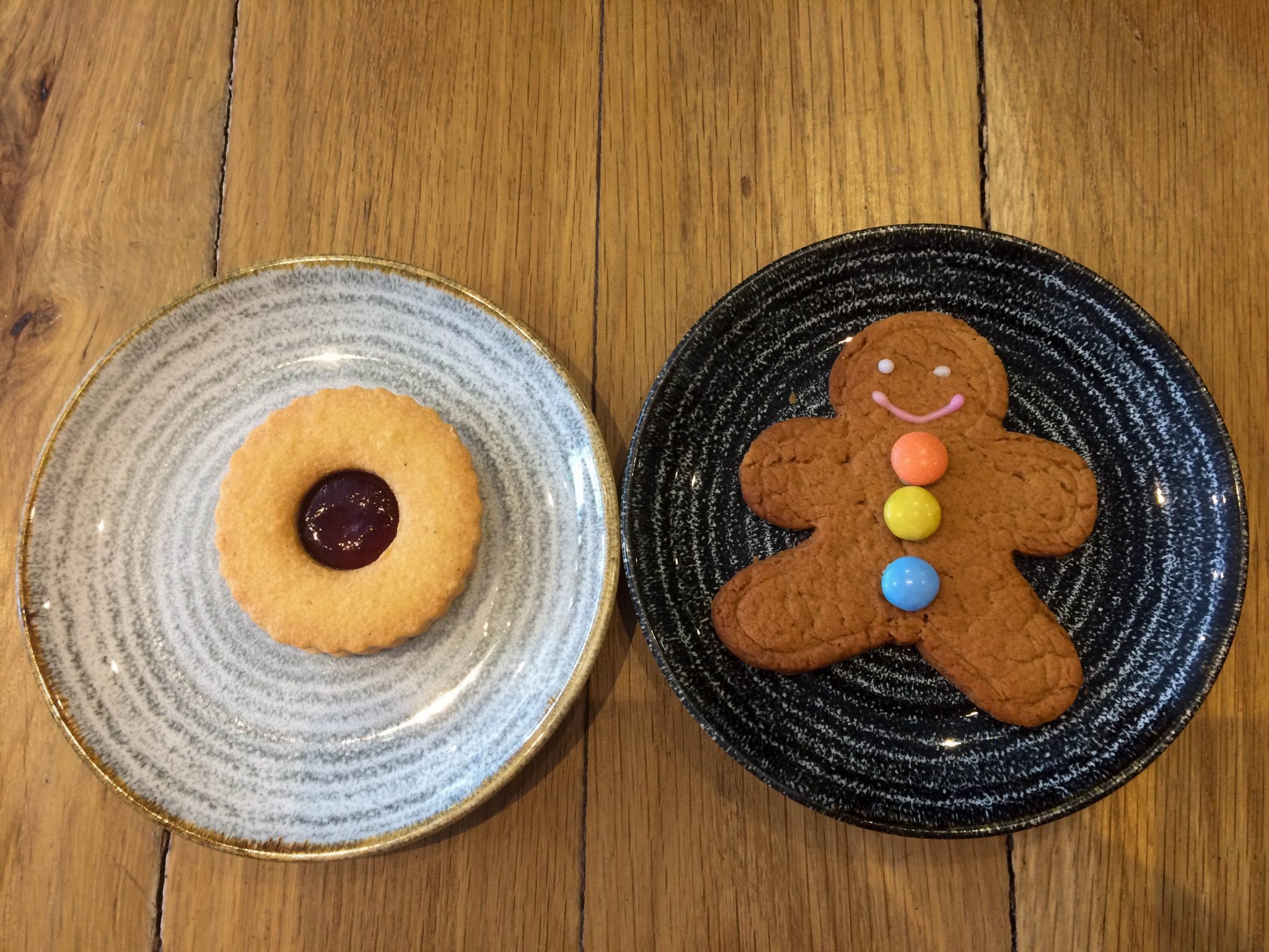 A ginger bread man and a jammy biscuit, each on its own plate.