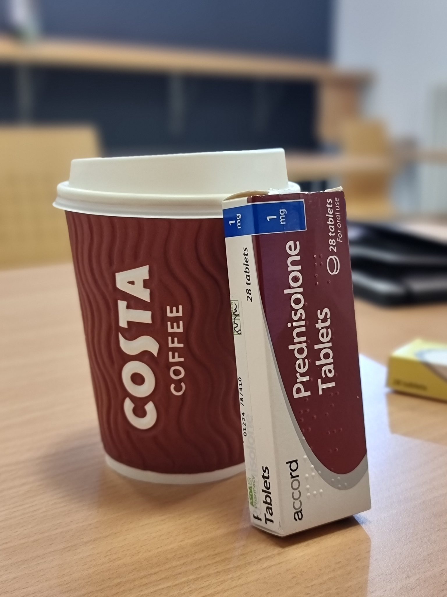A photograph of a box of steroid medication resting against a takeaway cup of coffee