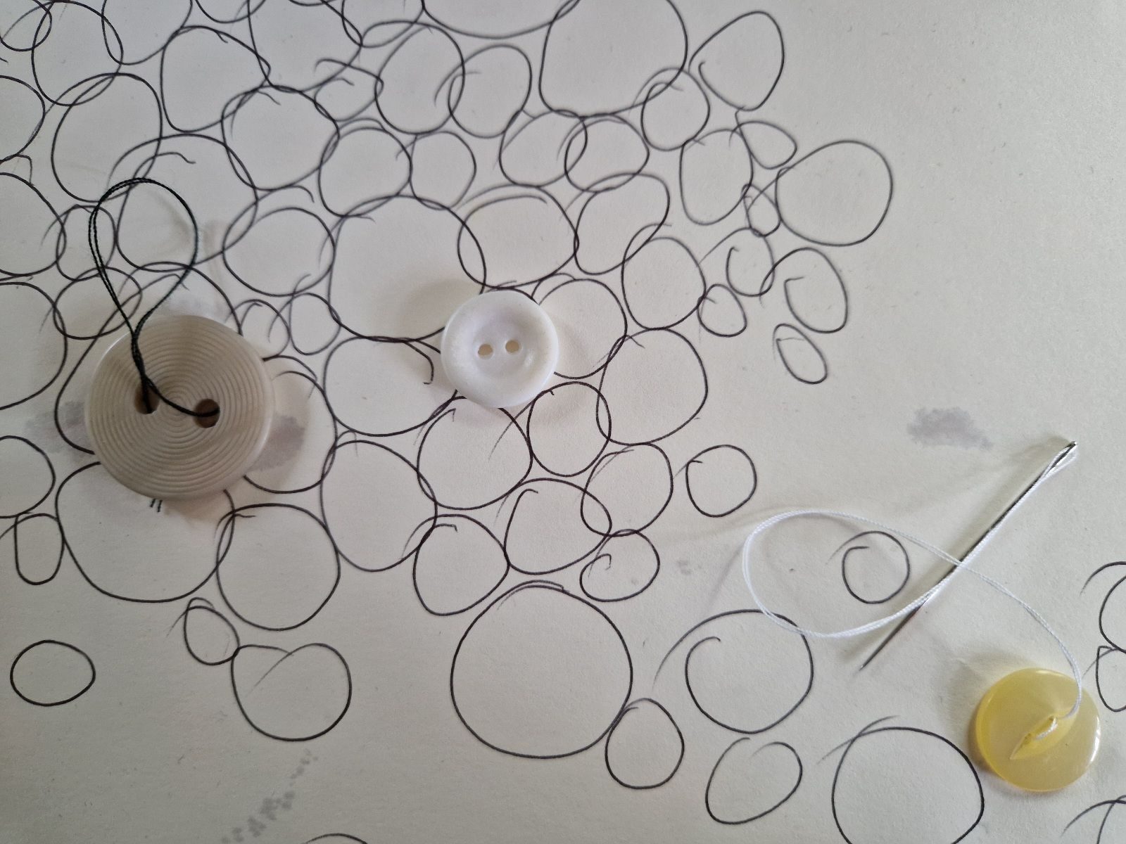 Circle line drawings in various sizes like bolders with 3 plastic buttons in the process of being sown into the fabric of the artwork