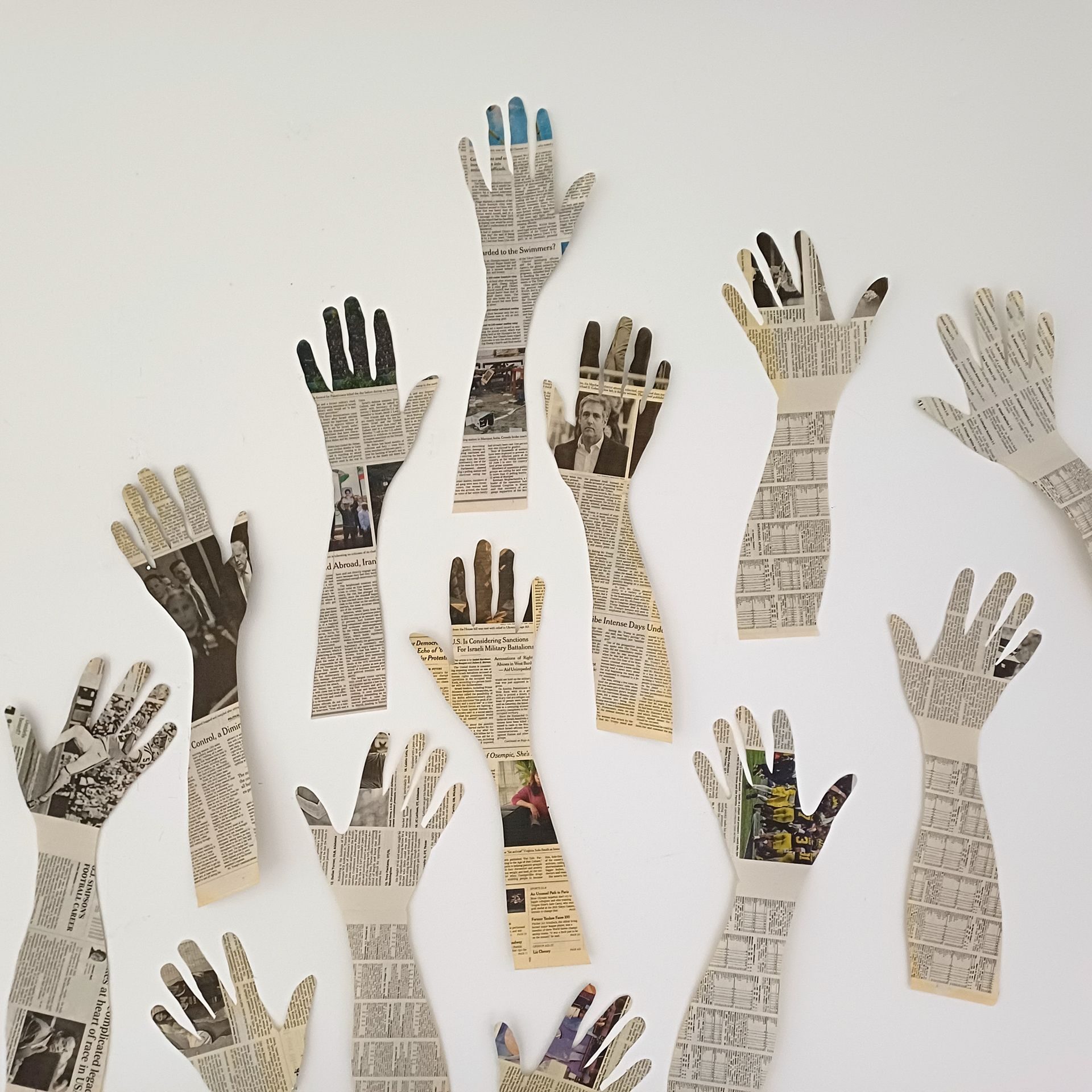 Cut out hands made from newspaper are placed on a wall reaching up, perhaps waving or calling attention to themselves.