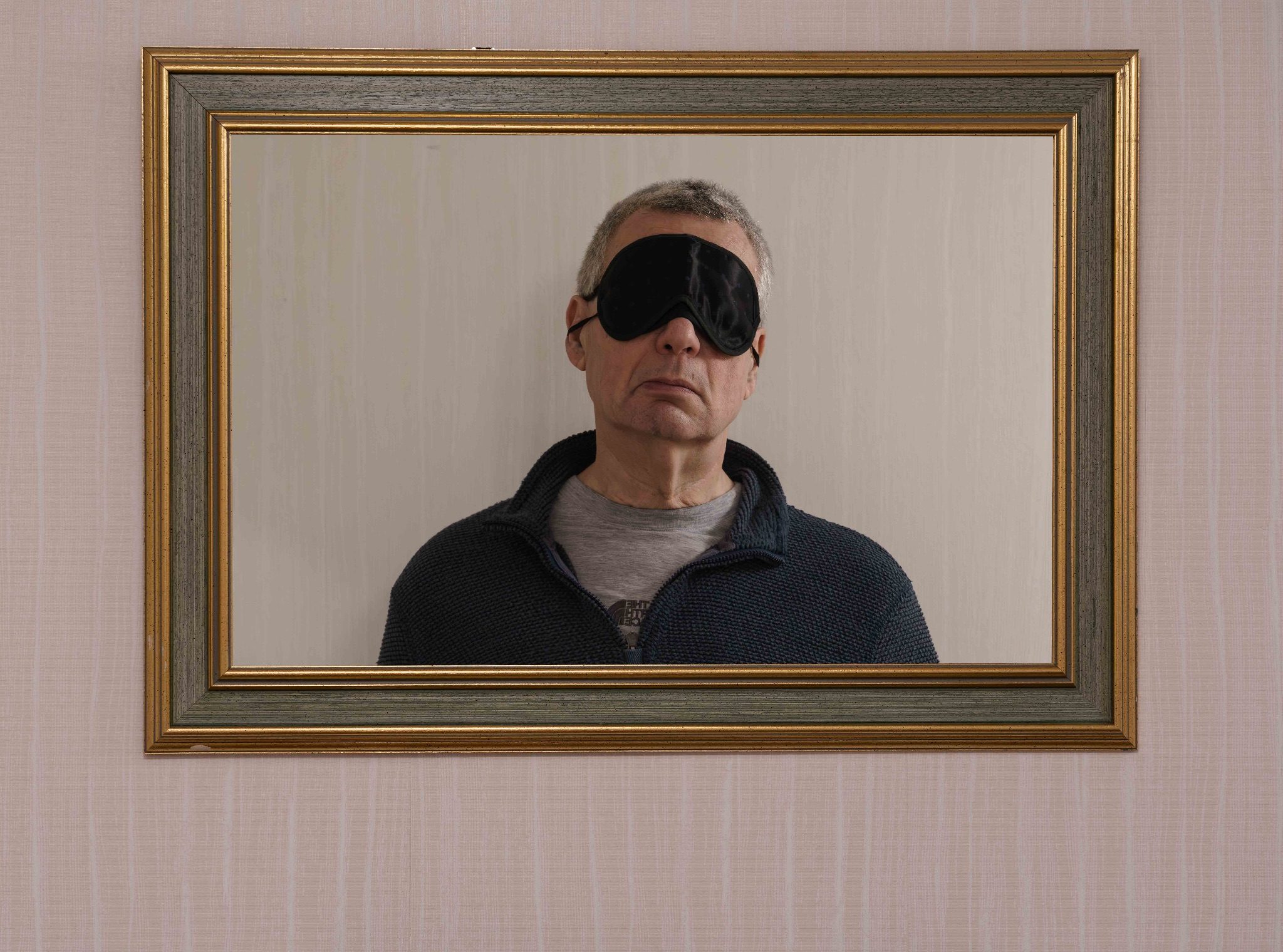 An image of a man, reflected, in a mirror with a sleeping mask over his eyes