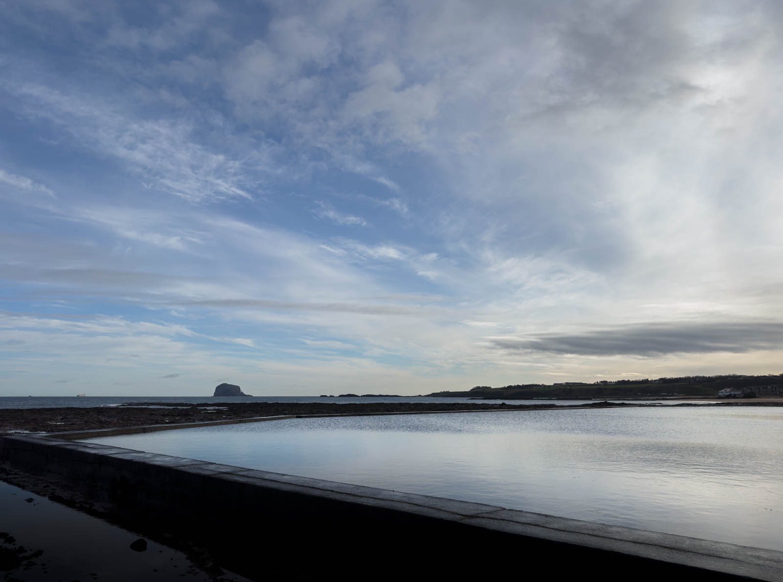 A photograph of a tidal pool with Bass Rock on the horizon