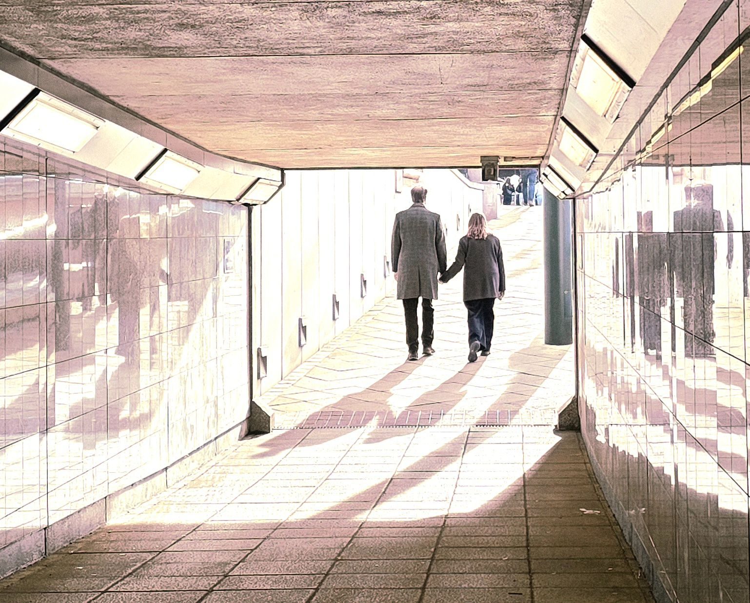A couple holding hands walking away from the viewer with shadow and reflection