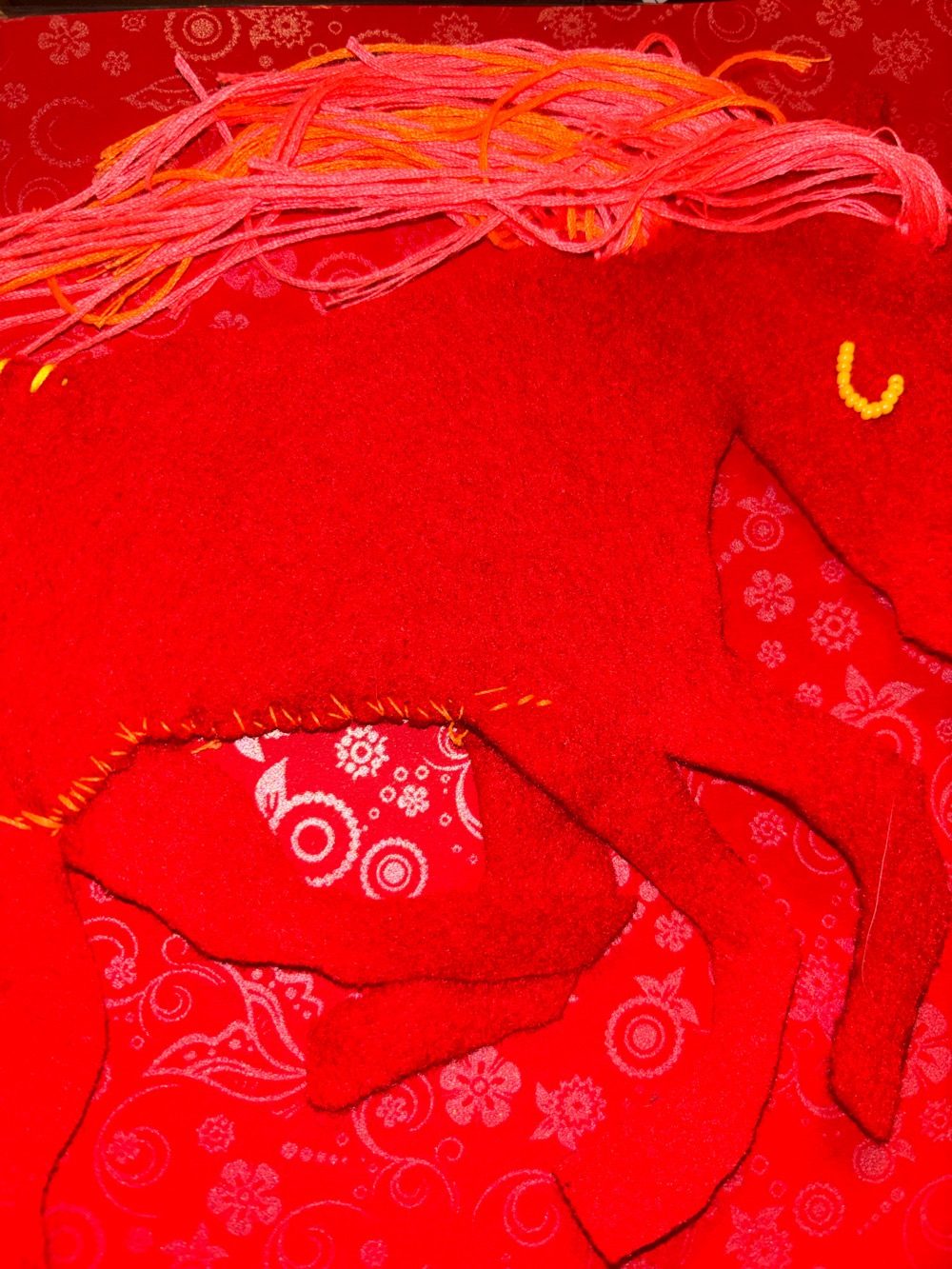 A felt horse with threaded hair on a floral red background