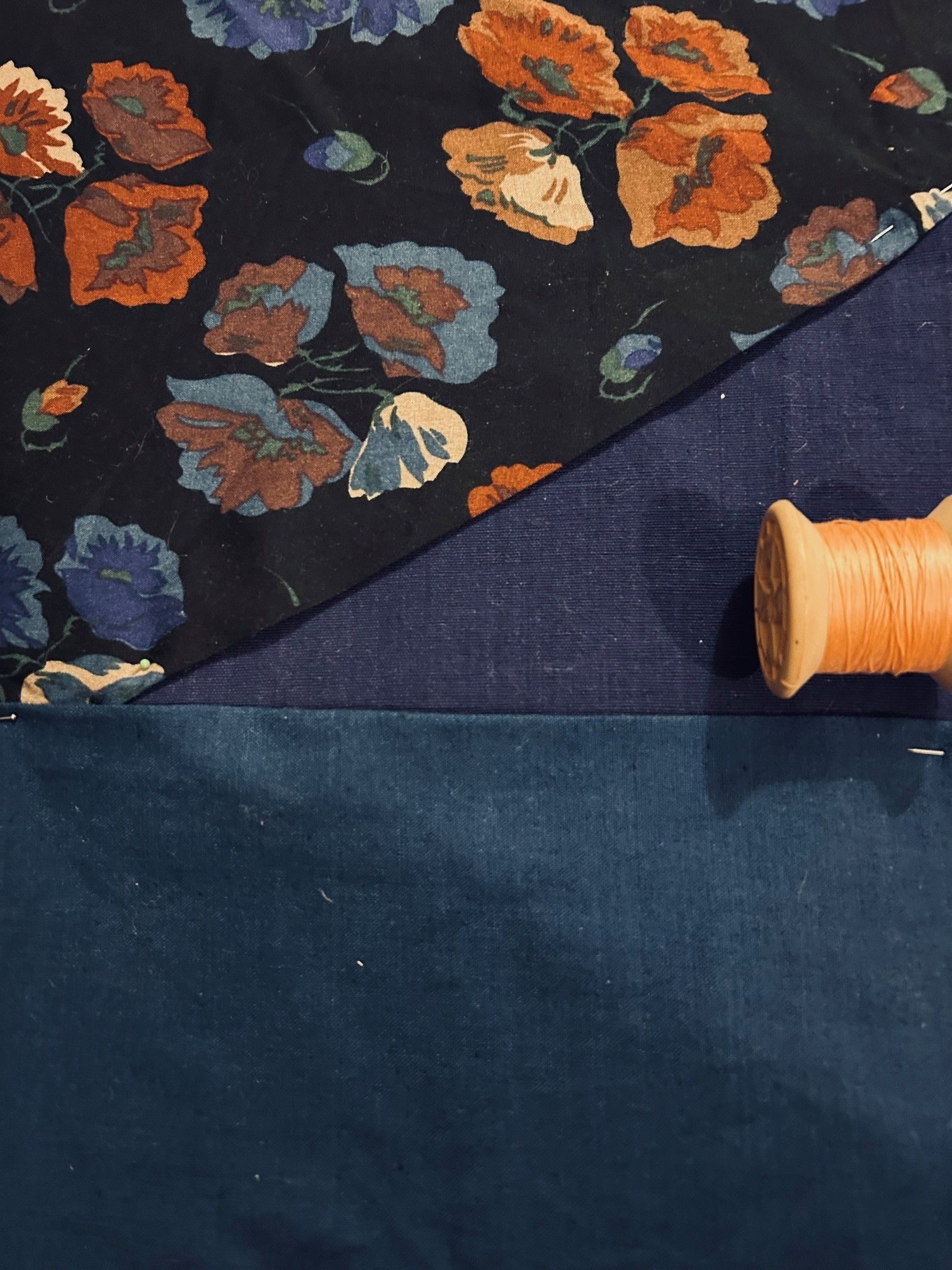 Three different pieces of fabric next to each other, one floral the other two shades of blue and some pink thread.