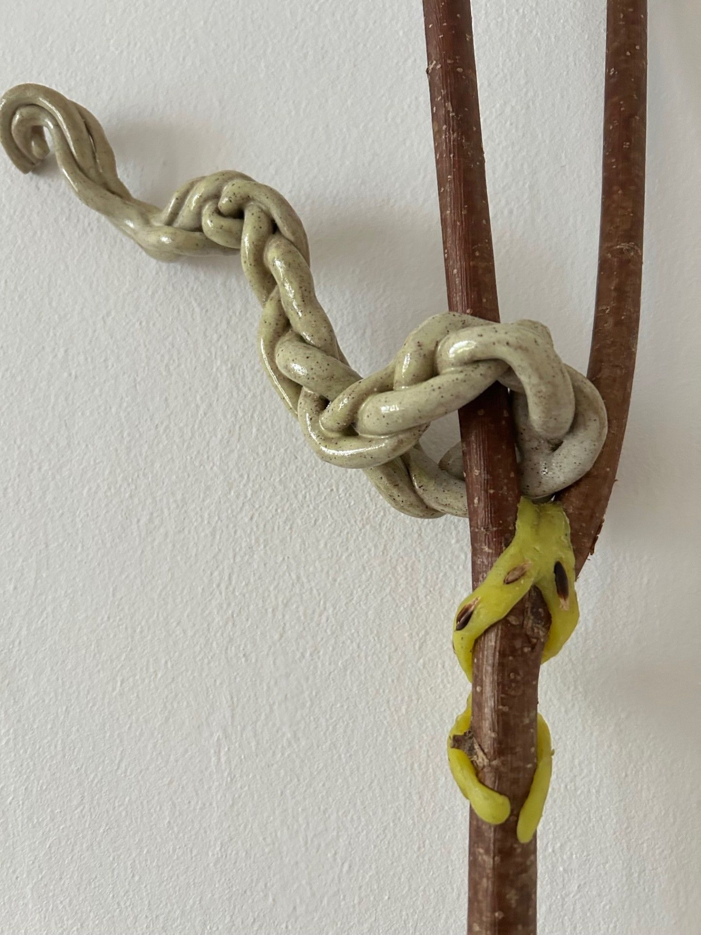 ceramic plat on the top of a forked stick, the plat looks like it is blowing in the wind. Beneath the plat is some twisting yellow wax with seeds pressed into it