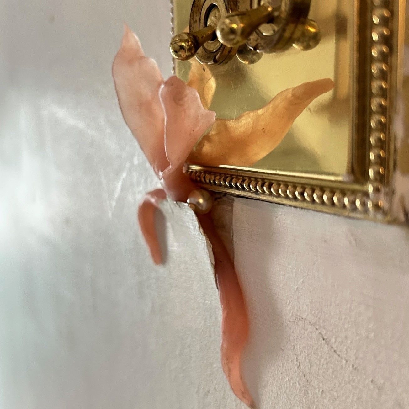 Wax creeping plantlike form emerging from a tear in wallpaper beneath a light switch. Shining out from the crack is a pearl that the form is carrying