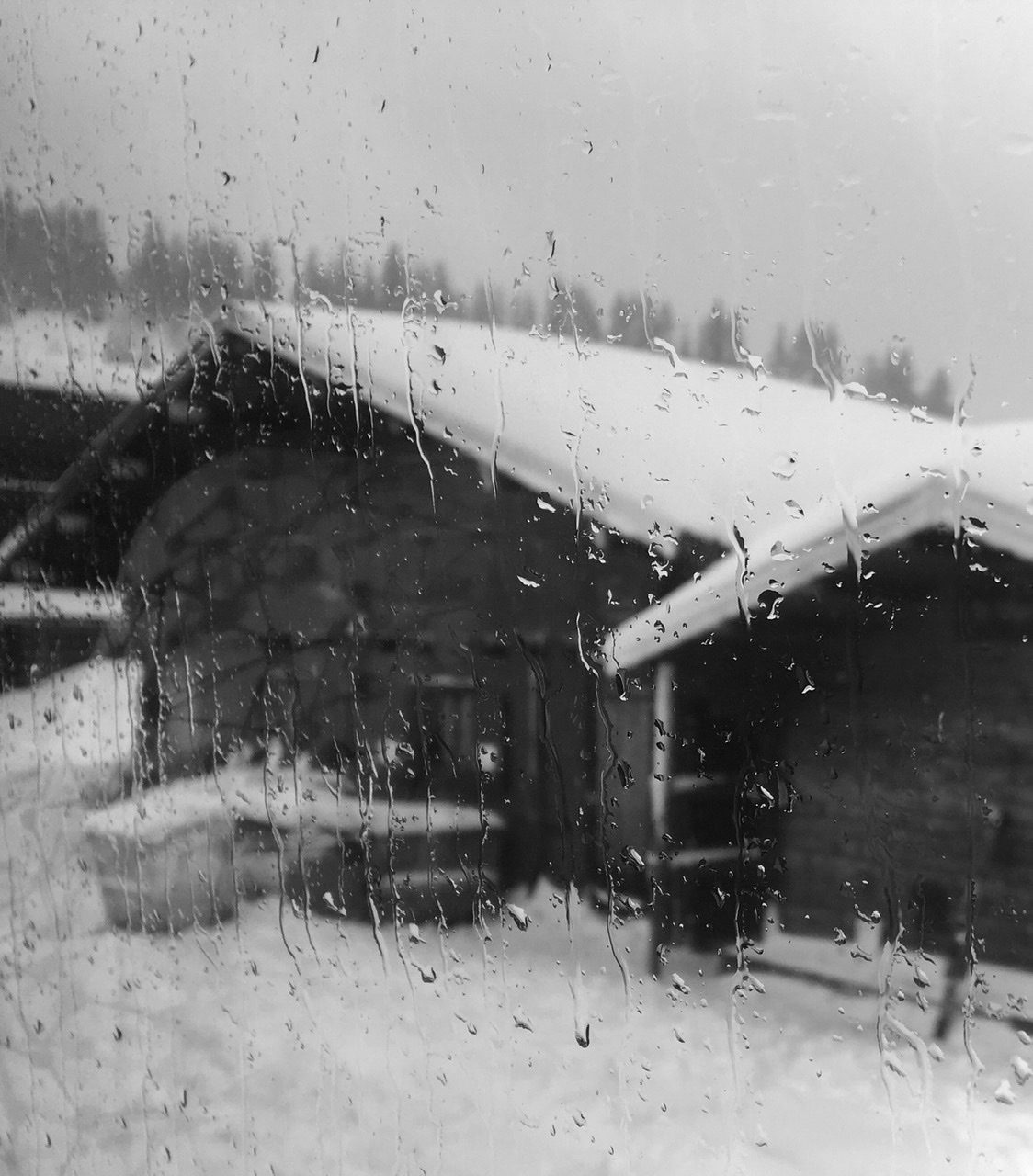 View through a rainy window onto 2 snow covered mountain huts
