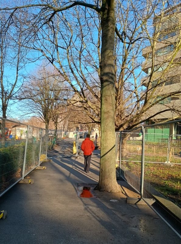 Man in a red jacket walking down a pathway between trees near London Bridge