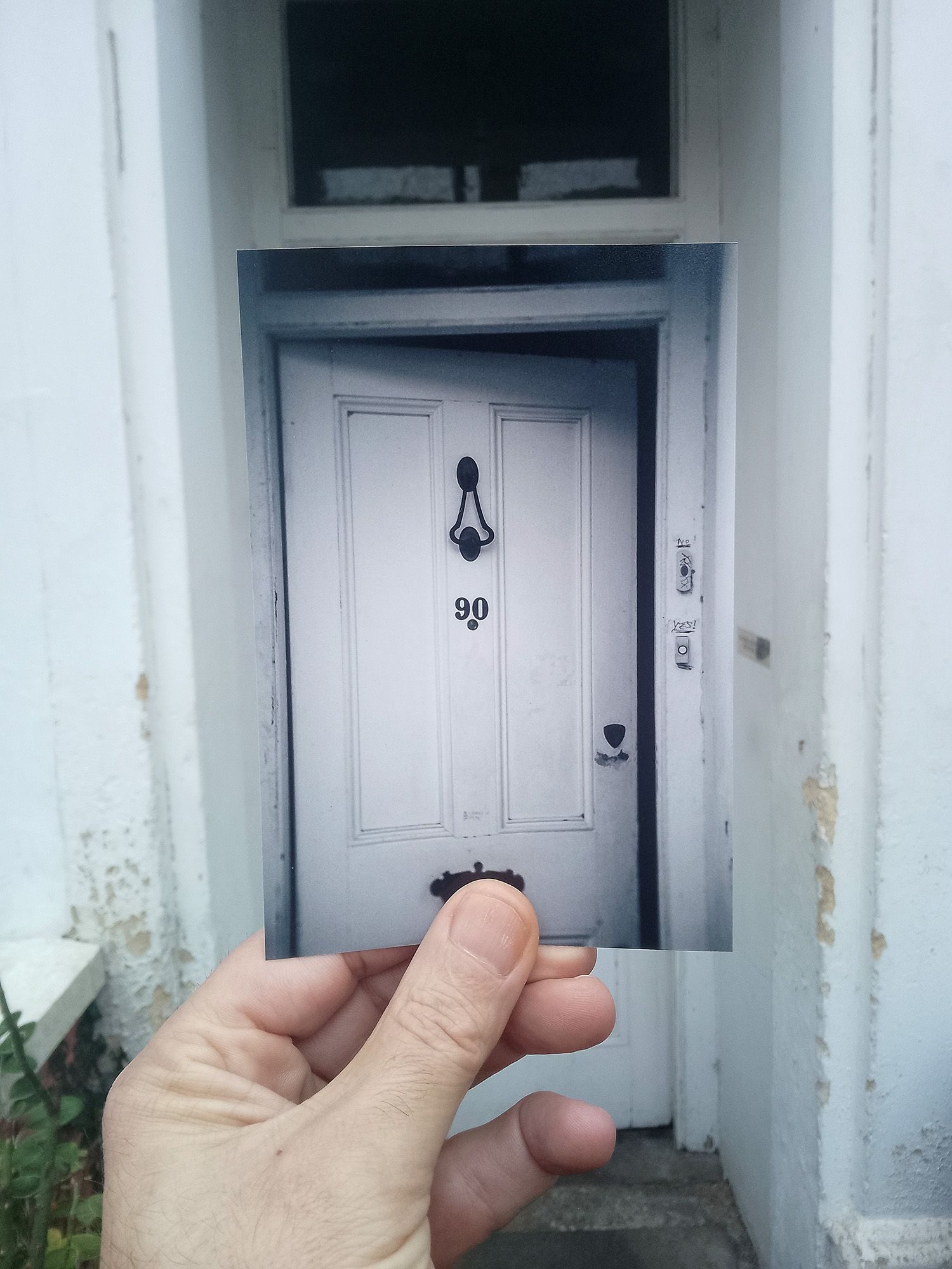 Photograph of my hand holding an image of the front door in front of the door.
