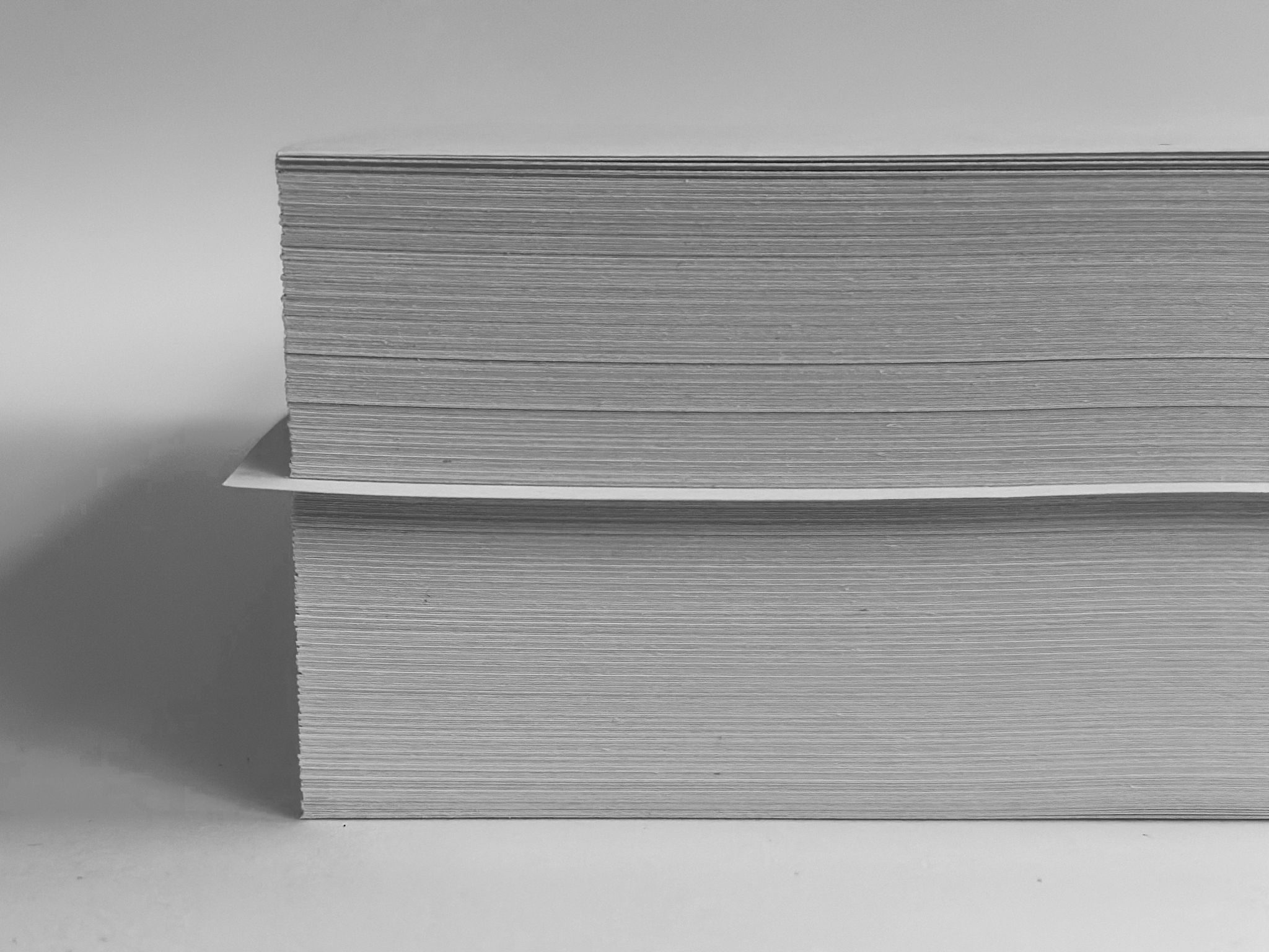 Black and white photograph of stack of A4 computer paper with one sheet out of place