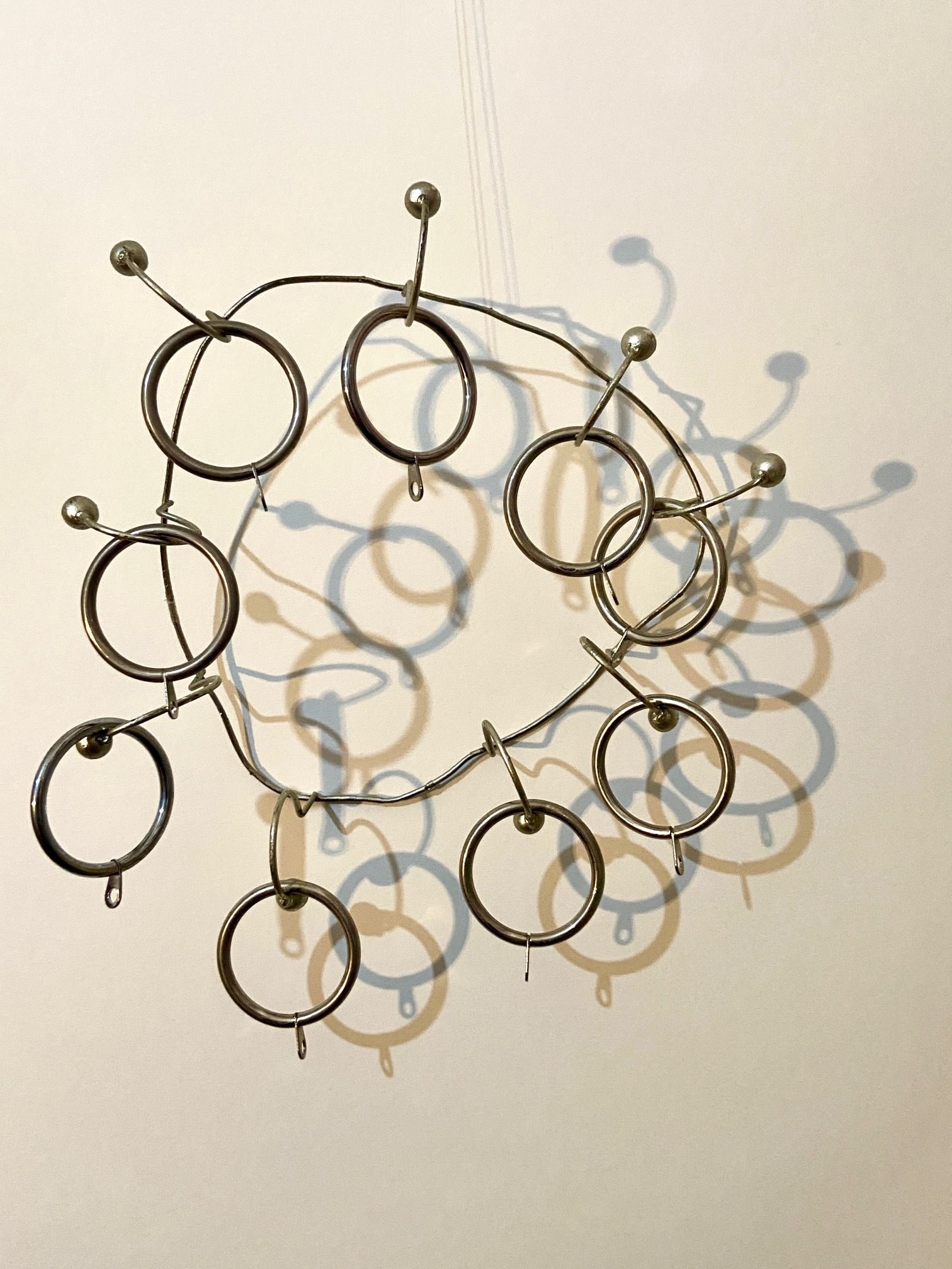 a wire form with 9 pegs holding curtain rings, lit to give curious shadows