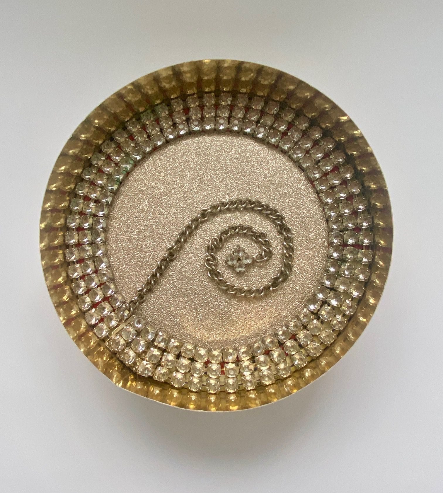 a diamond belt, curled around a circular gold box, with it's chain reaching out into the centre space as a spiral