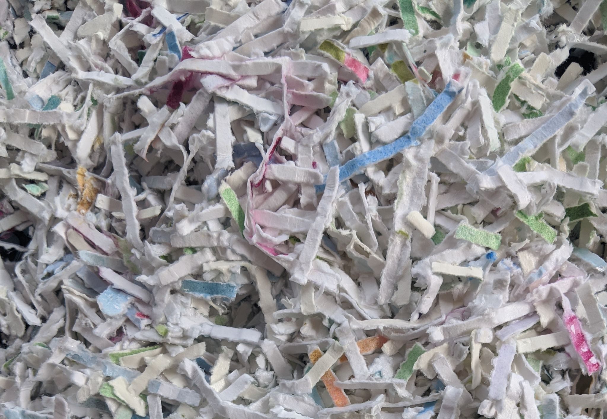 top view of shredded watercolour paper, mainly white and intercepted by shreds of colour