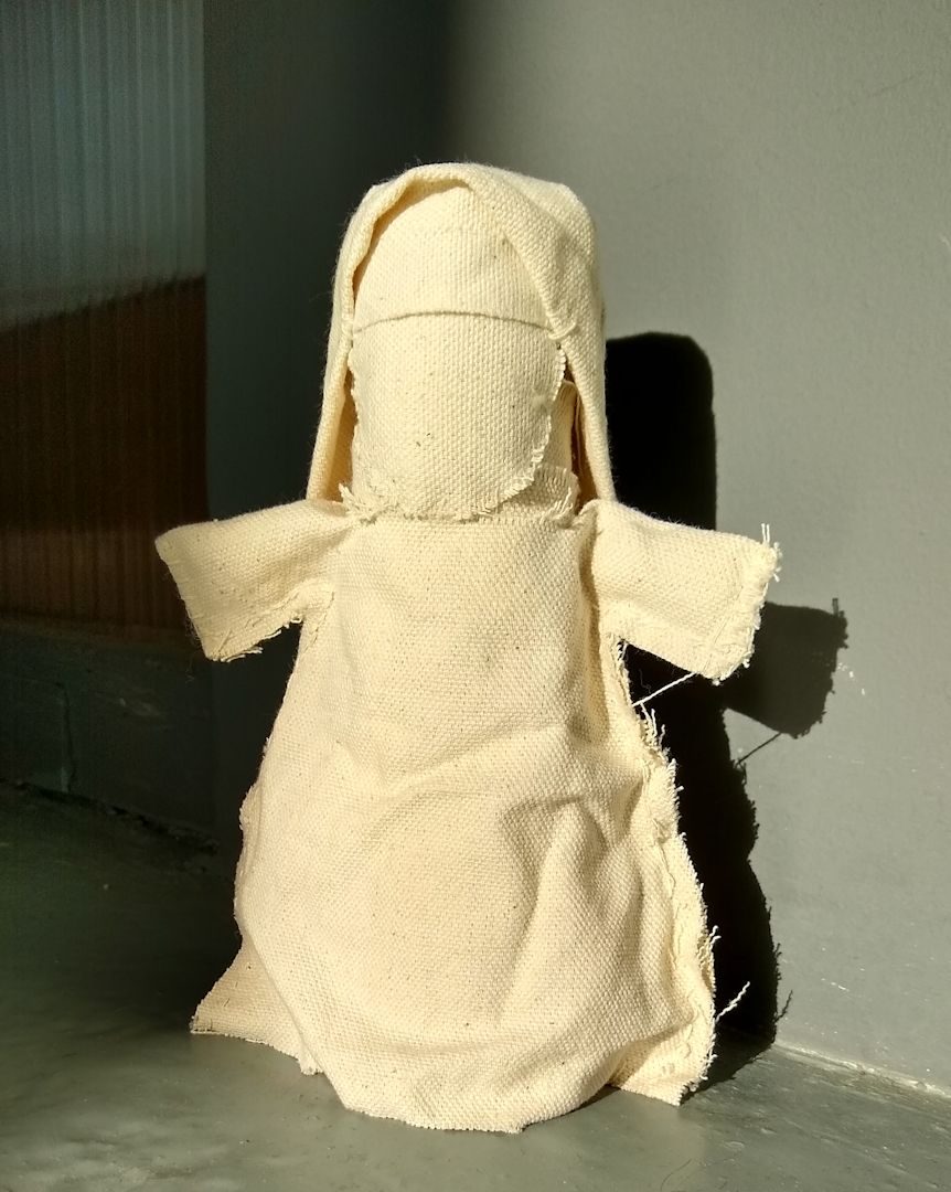 A doll made of cream cotton duck fabric. the doll has a blank canvas face and is dressed like a nun or an olden days nurse, in a long cream dress and a headscarf.