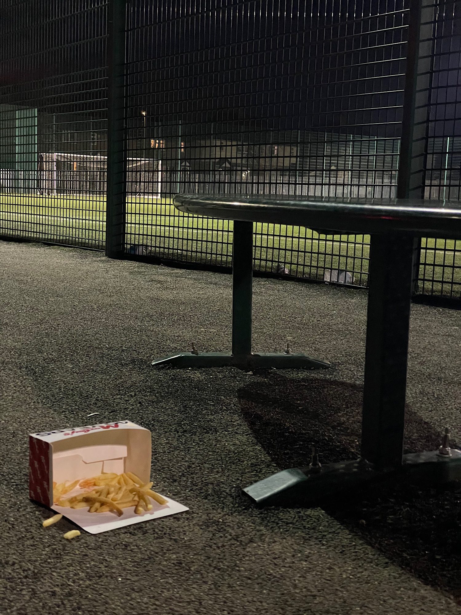 A nighttime photo of a fallen box of chips near a green metal bench