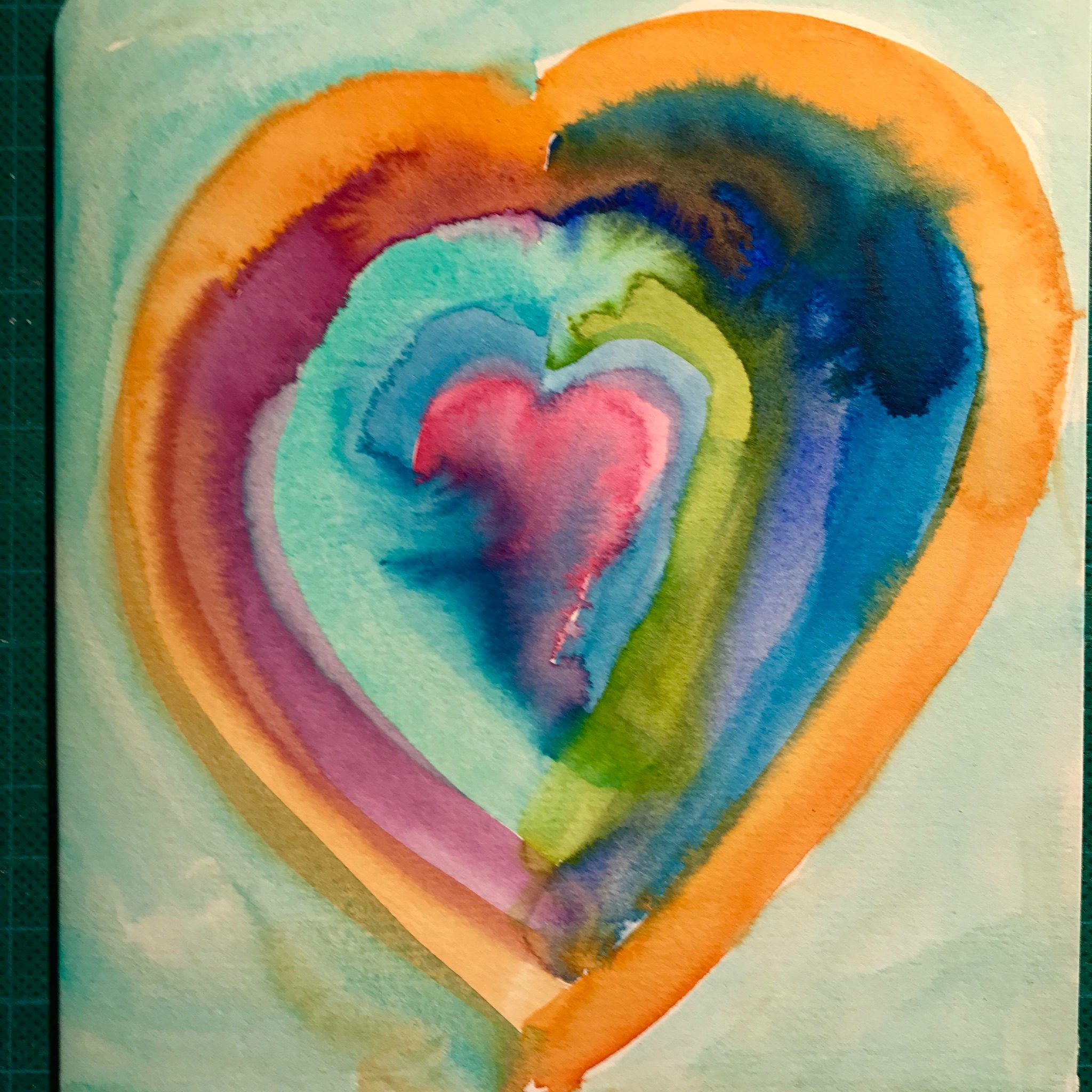 a pink watercolour heart with bands of different wet watercolours around each side of it, all blurring into each other - blue, orange, and turquoise with a little green and ultramarine. with a light turquoise background.