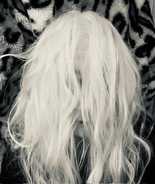 black and white photo of a head, long white hair covering the face, leopard print fur fabric background