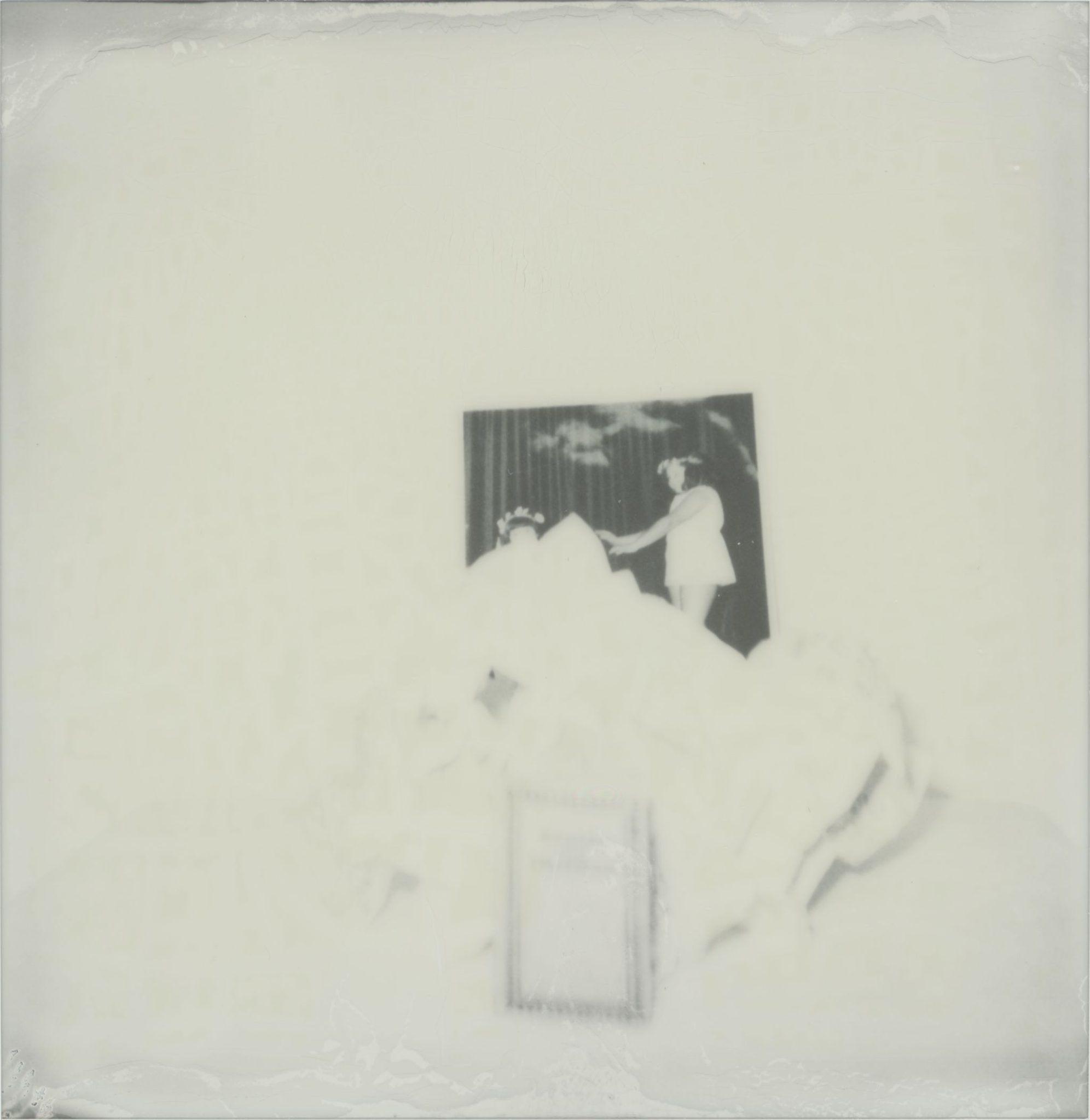 Black and white polaroid image - distorted still life with paper pile and old photographer of two sisteres