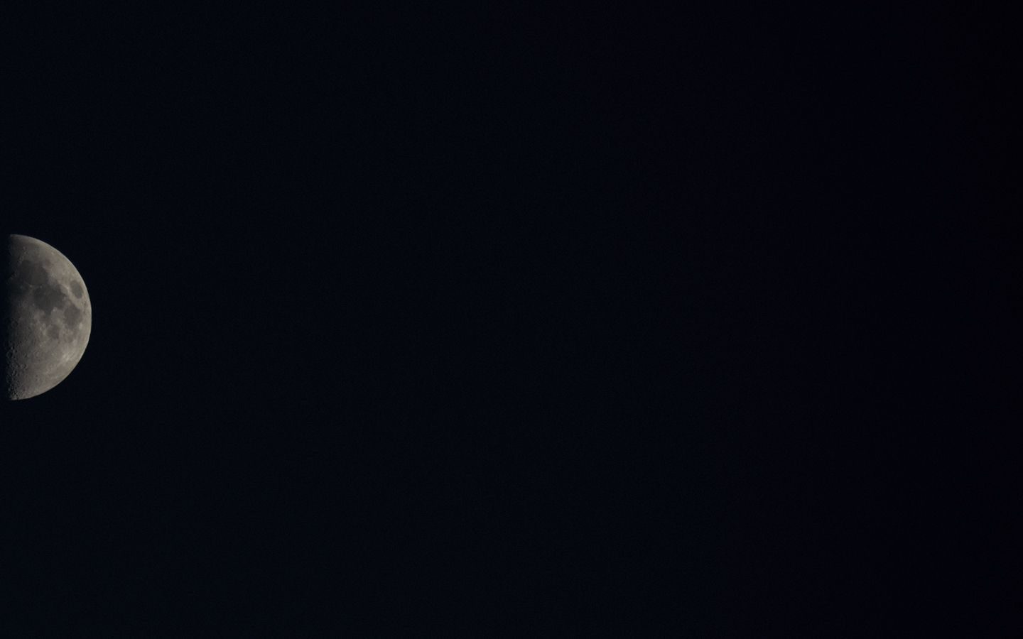 a mostly black photograph with a waxing half moon set at the far left