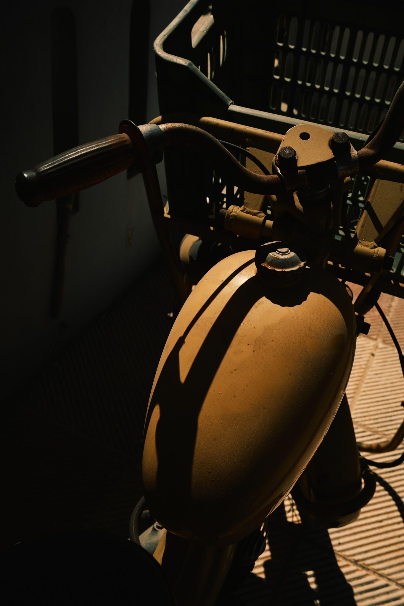 Colour photograph of an old yellow motorcycle. Dark image with crushed shadows and warm tones