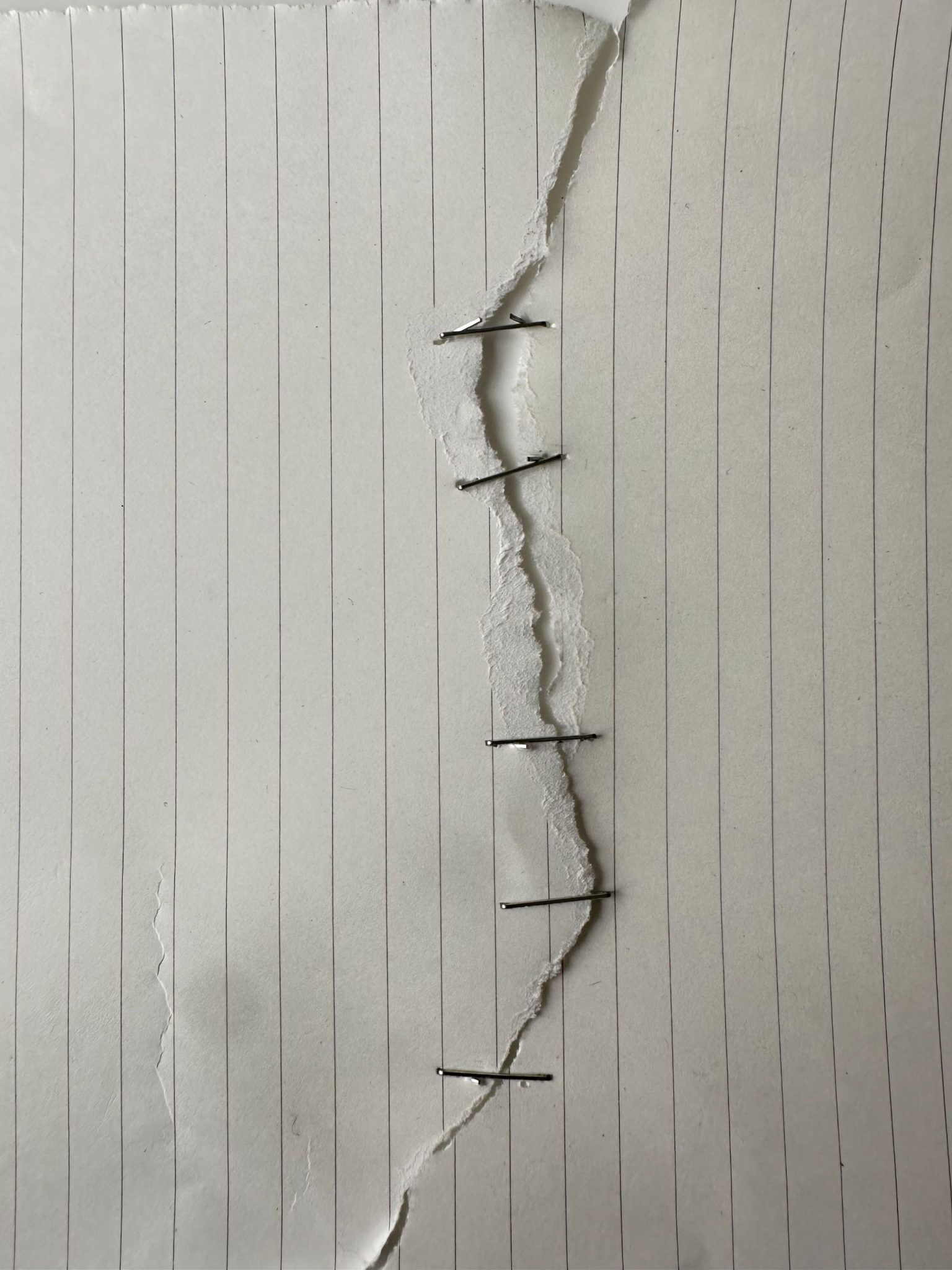 Piece of lined paper torn in half and stapled back together.