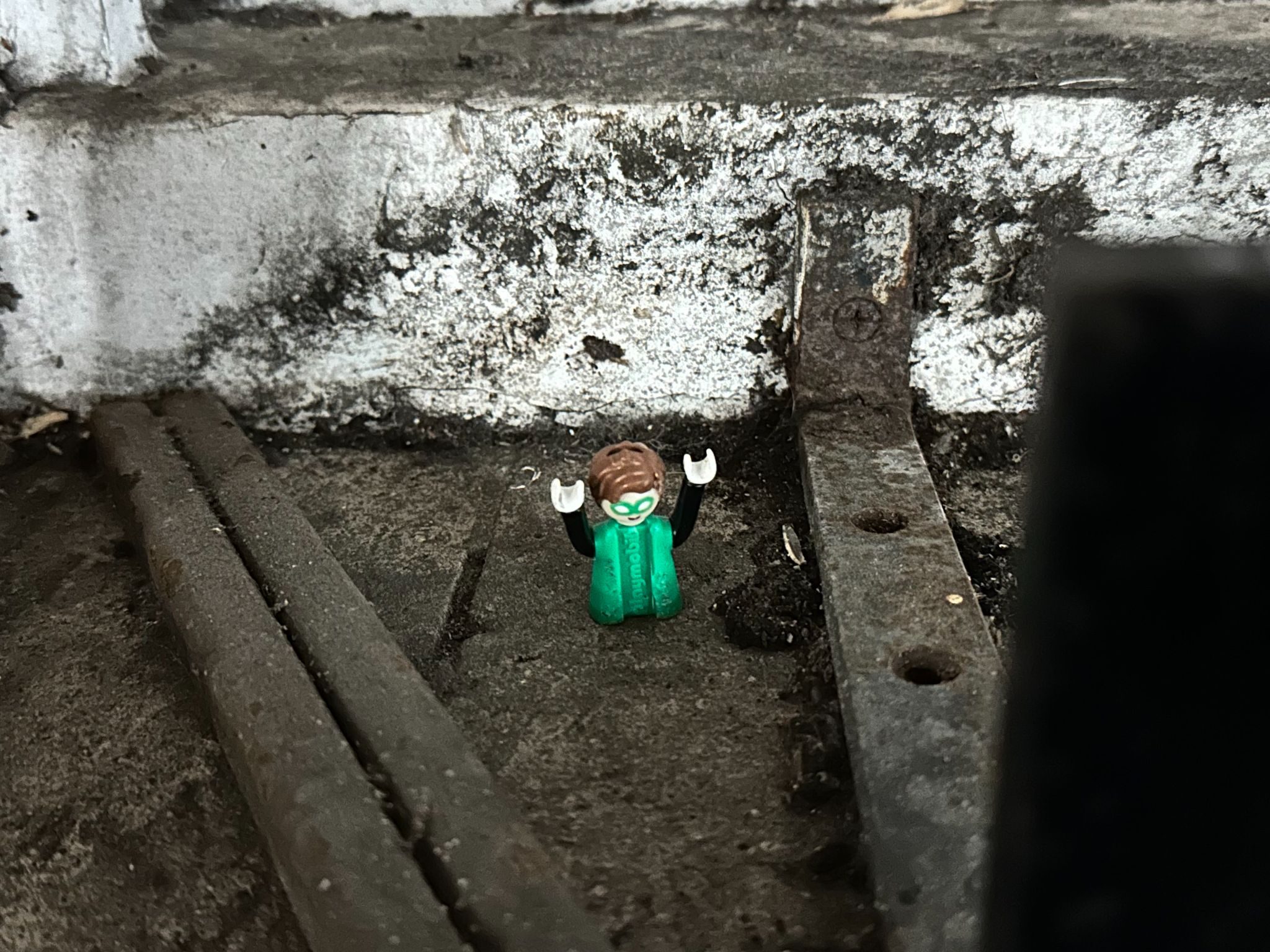 Top half of small green Playmobile figure sitting in an urban environment