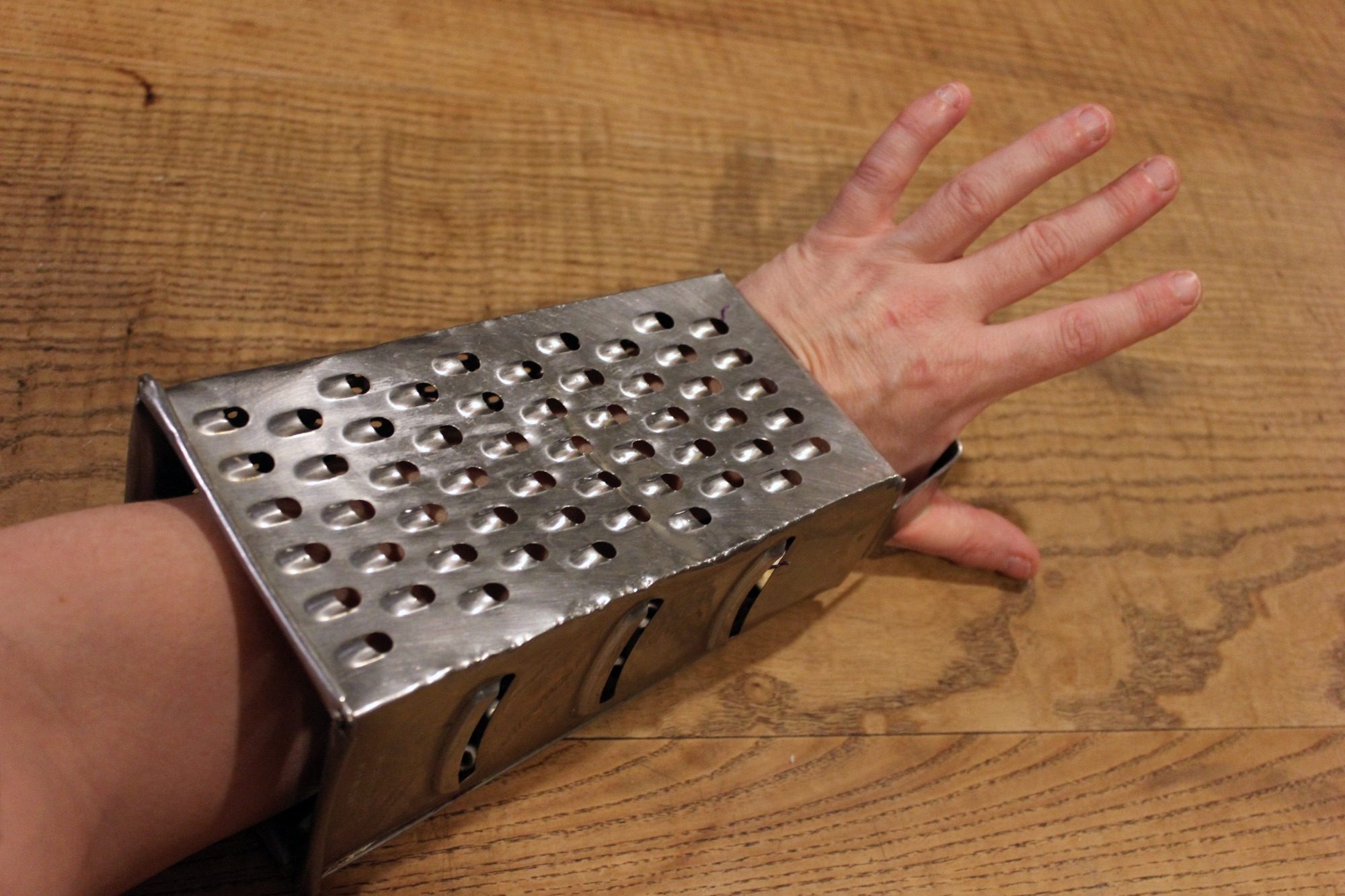 My arm is inserted into a four sided box grater. My hand pokes out the top by the handle.