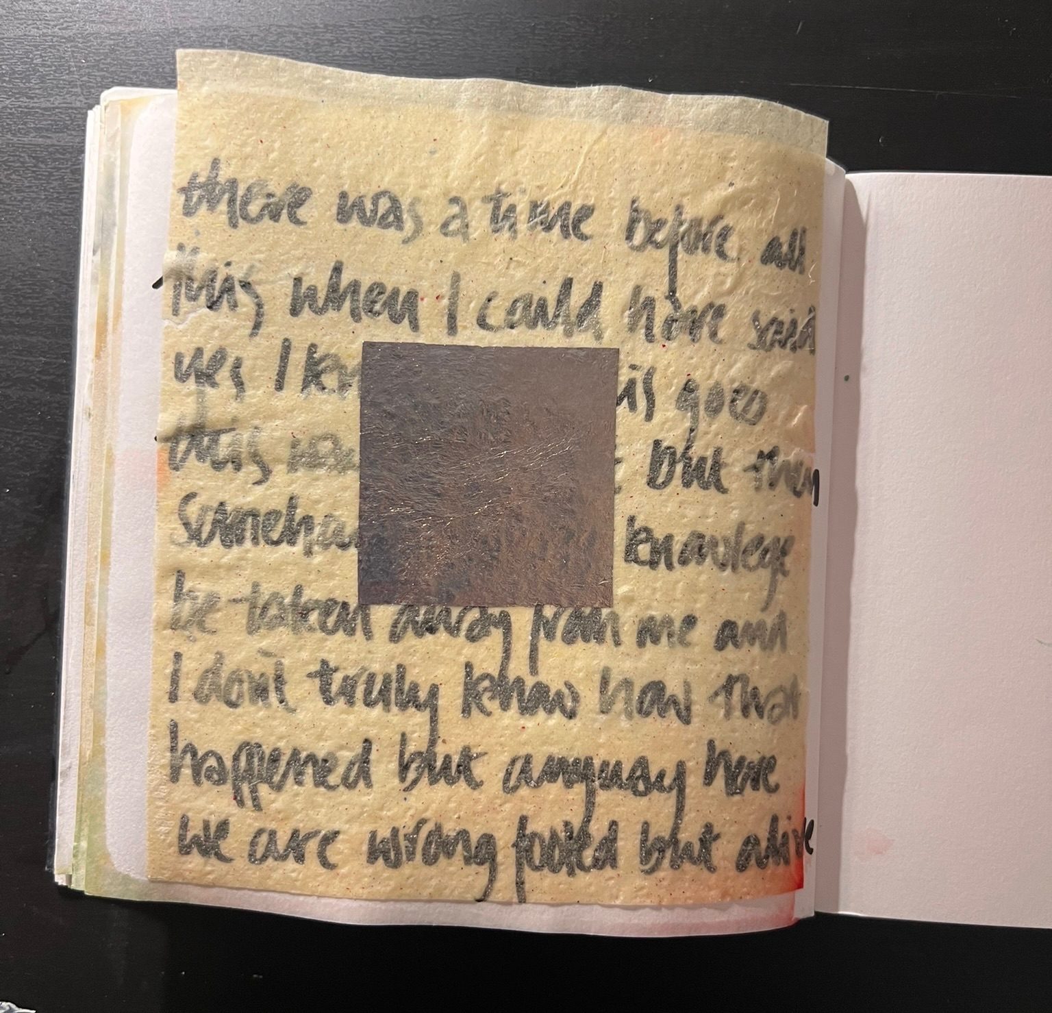 Black script on white paper with yellow paper overlaid and surface silver square