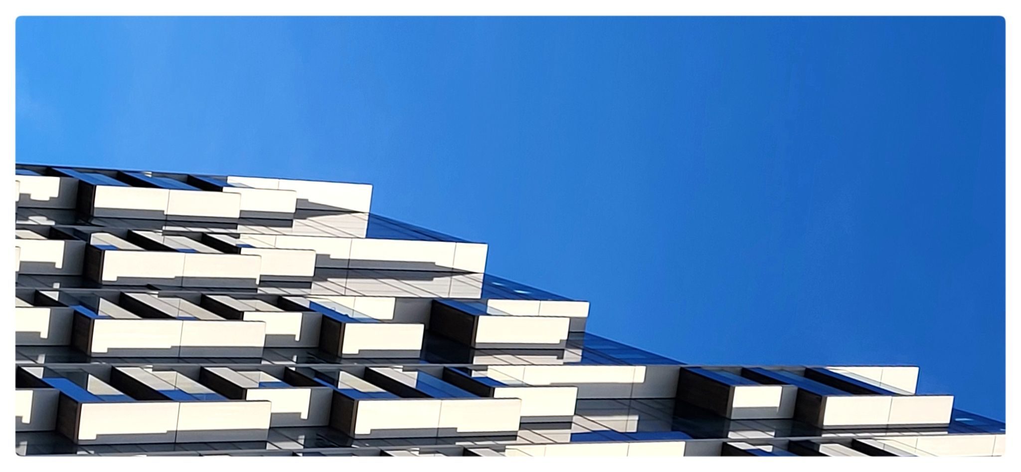 A flipped photo of a modern glass building against a blue sky