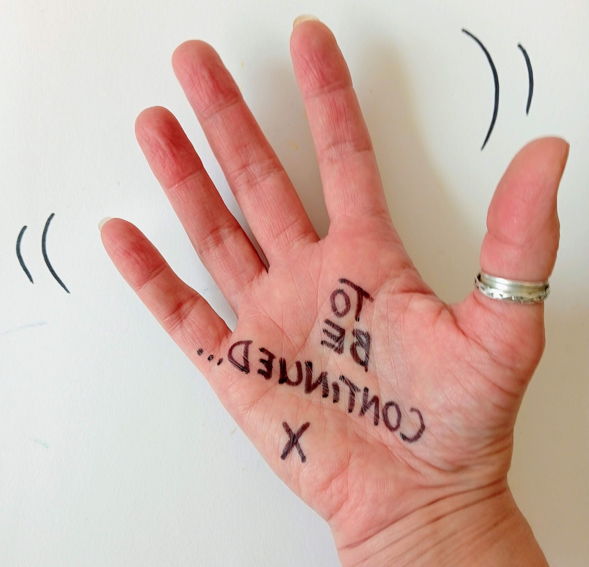 Square photographic image of a hand waving. There are motion marks on either side of the hand and the handwritten message 'To be continued' appears backwards across the palm