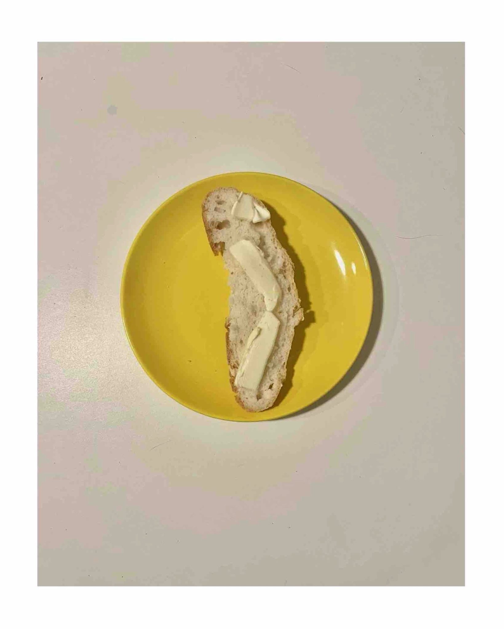 A photo of a piece of gluten free bread with lumps of butter on a yellow plate