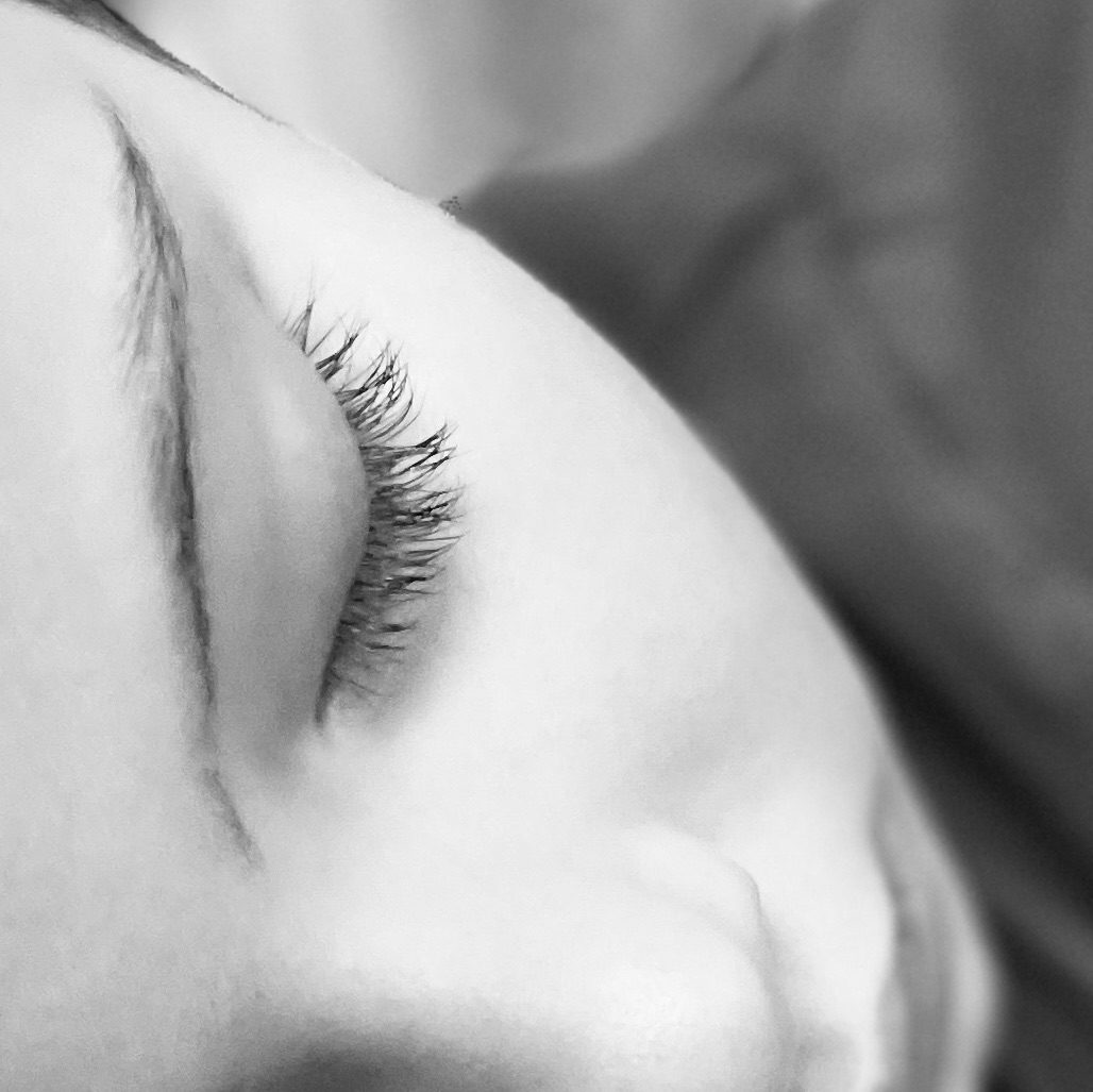A black and white close up photograph of half the face of a sleeping child, one eyebrow, closed eye, half a nose and a closed mouth, almost abstract in appearance.