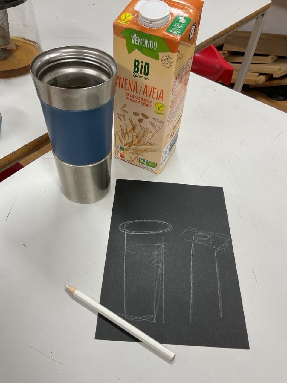 A quick line drawing of a cup and milk carton in white pencil on black paper. The objects are part of the photograph.