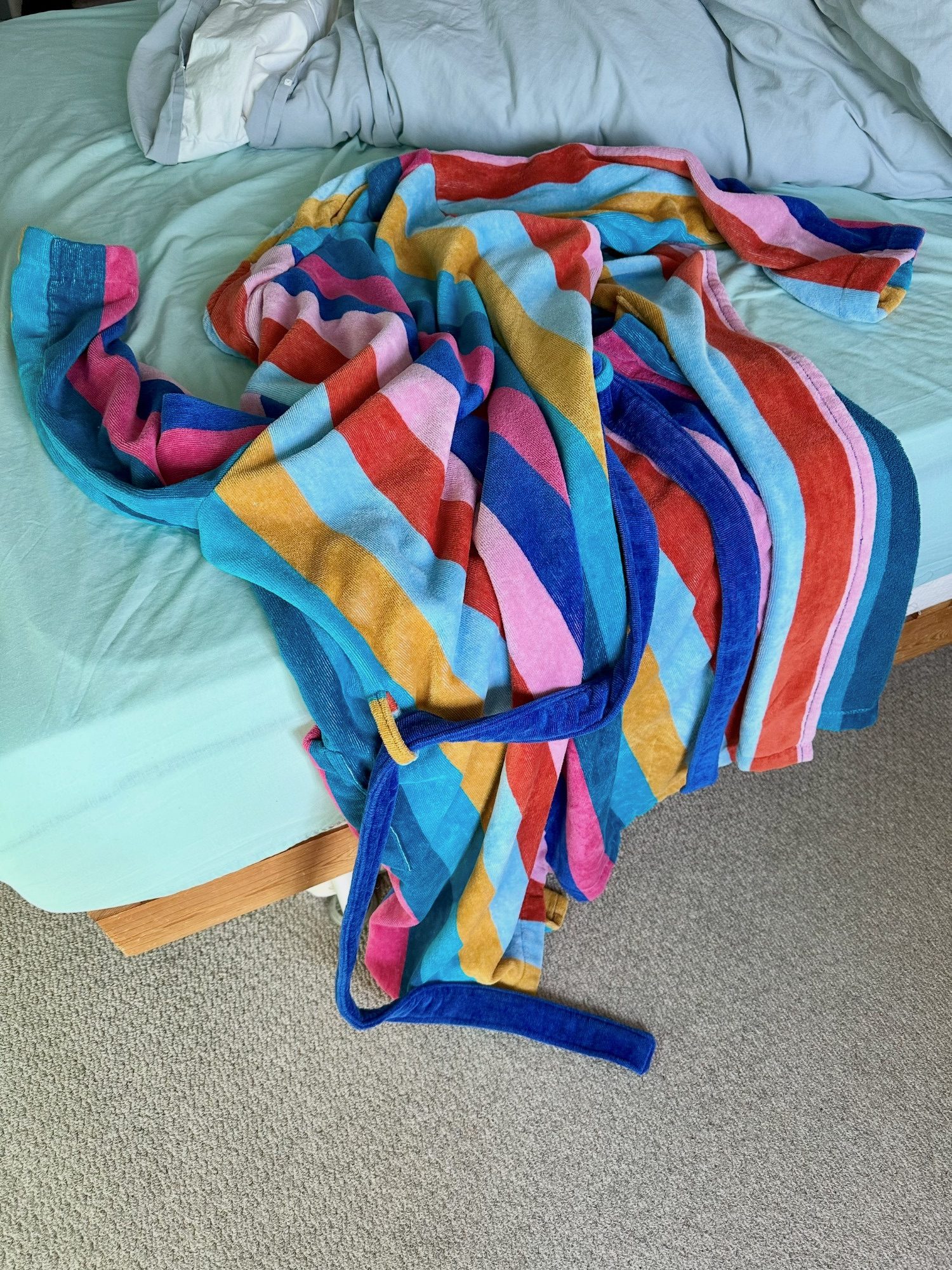 Photograph. Discarded multi colour striped dressing gown on unmade bed.