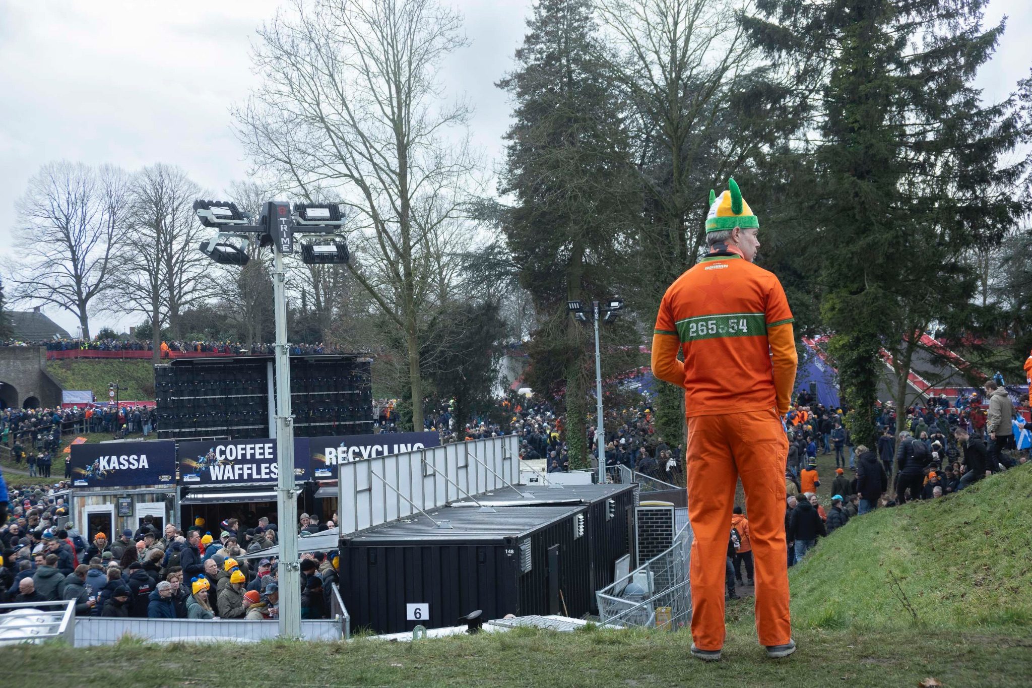 A man stands on a grass verge wearing a beanie hat