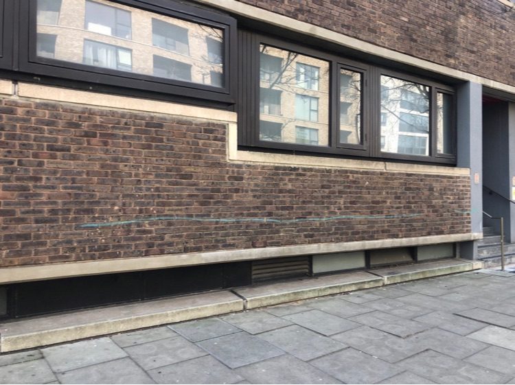 light green line sprayed along a university building. my understanding is this mark is the most basic and most quick way to deface.