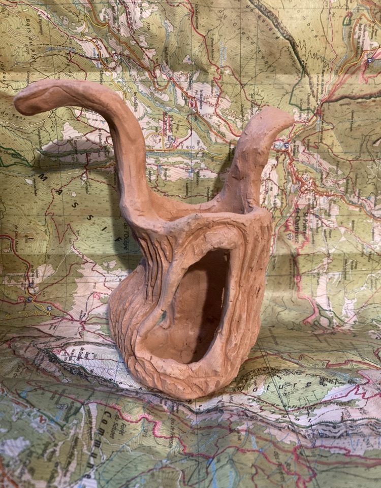 It is a clay sculpture of a tree this has 3 sides with great big holes in the trunk all around there is two mis-shaped branches that are only sticking out the sides above that look like a person that has their arms above their head in a flourish. It is bare and bleak there is detail on the bark of the tree with strokes of detail in the clay like bark it is a little swaying maybe resembles a surreal dream but it’s not really a play toy for a bird it’s what is left behind by people maybe after logging of the forest or of the fire where it’s just a burnt out tree with two main trunks. The Title is “Who Are We Kidding? The Birds And Beasts Should Know What We Are Doing.