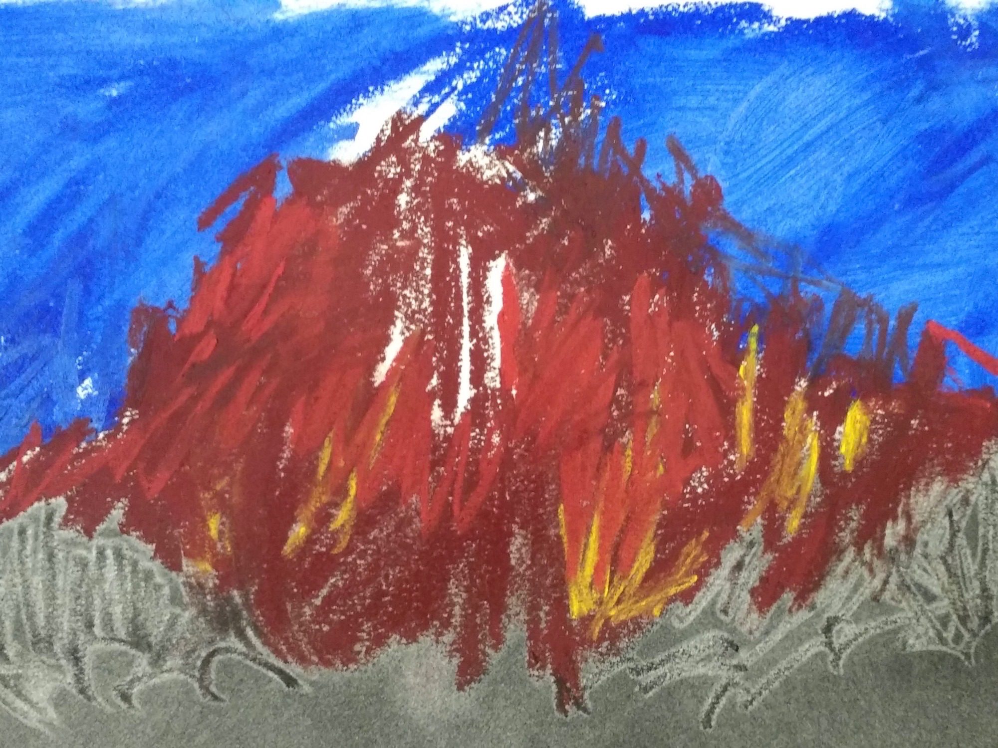 Scribbled mountain fire in scribbled soft pastel, shades of red, orange and yellow on charcoal ground which has a surf of marks which have disturbed the charcoal below the red. Above, a pale ultramarine sky.