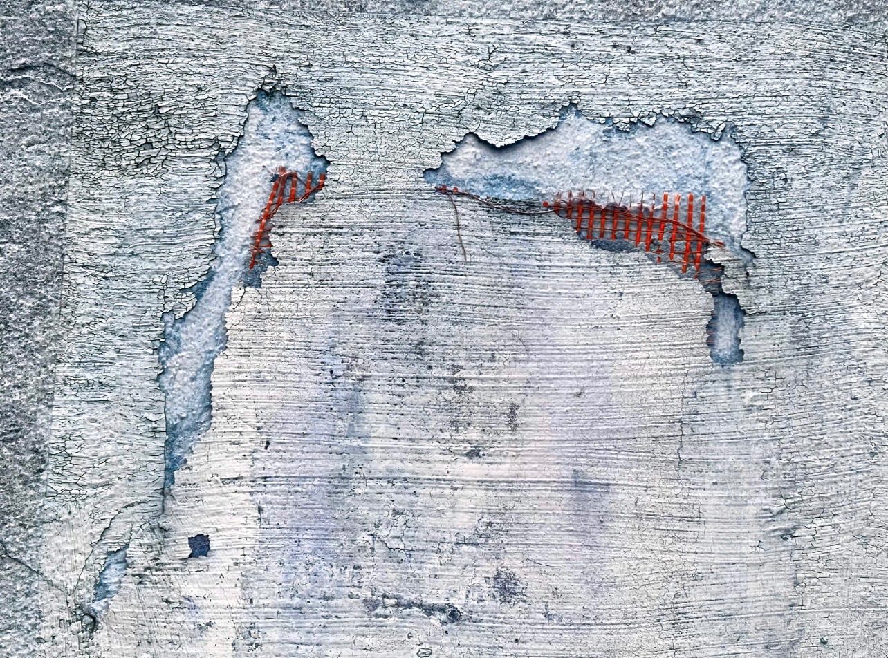 A minimalist photograph of an urban surface that resembles a distressed face. The peeling plaster forms hollow eyes and a mouth, revealing a vibrant orange mesh beneath. It is a haunting study of structure and decay, where a cold wall seems to take on a human expression of vulnerability and silent protest.