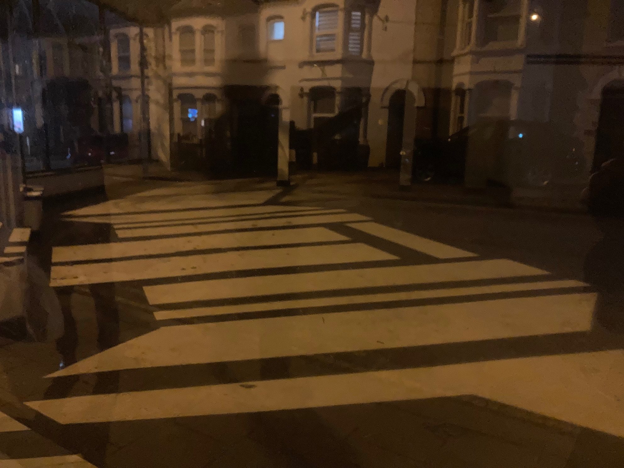 A photo of the reflection in a window of a street but you can also see the interior of an empty shop with geometric shadows on the floor