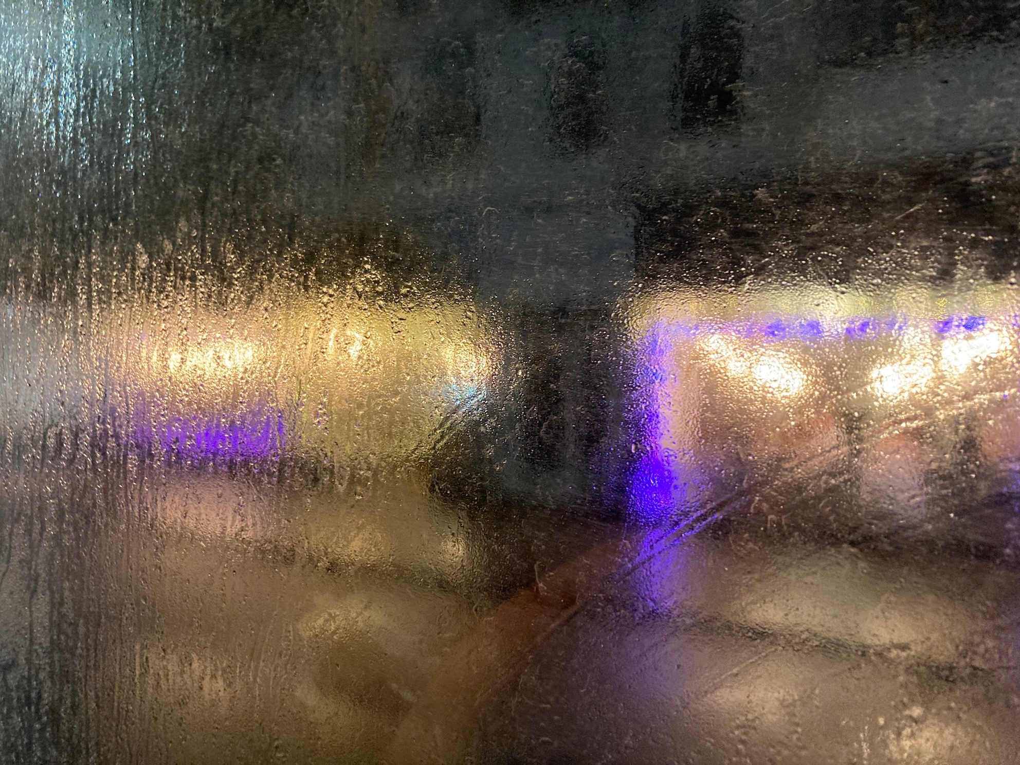 A photo through a rainy bus window of a bar with purple lights